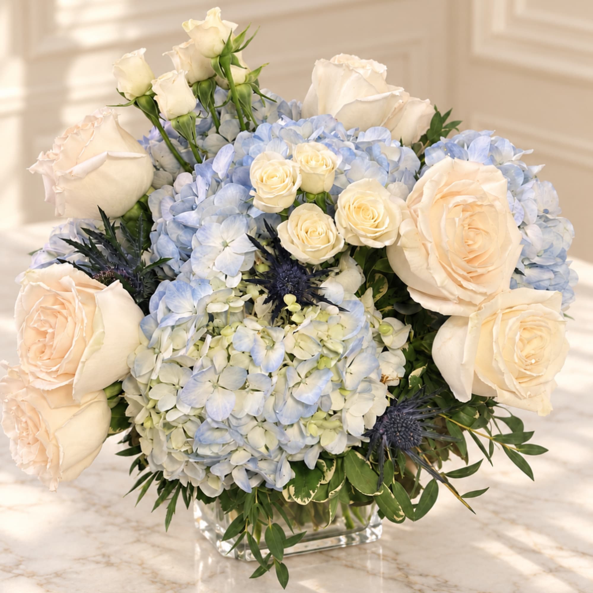 Cream roses and blue hydrangeas arranged in a clear square vase