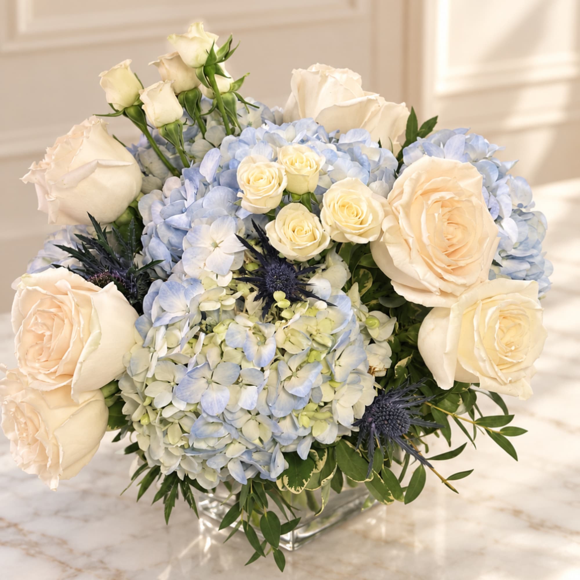 Cream roses and pale blue hydrangeas in a clear square vase
