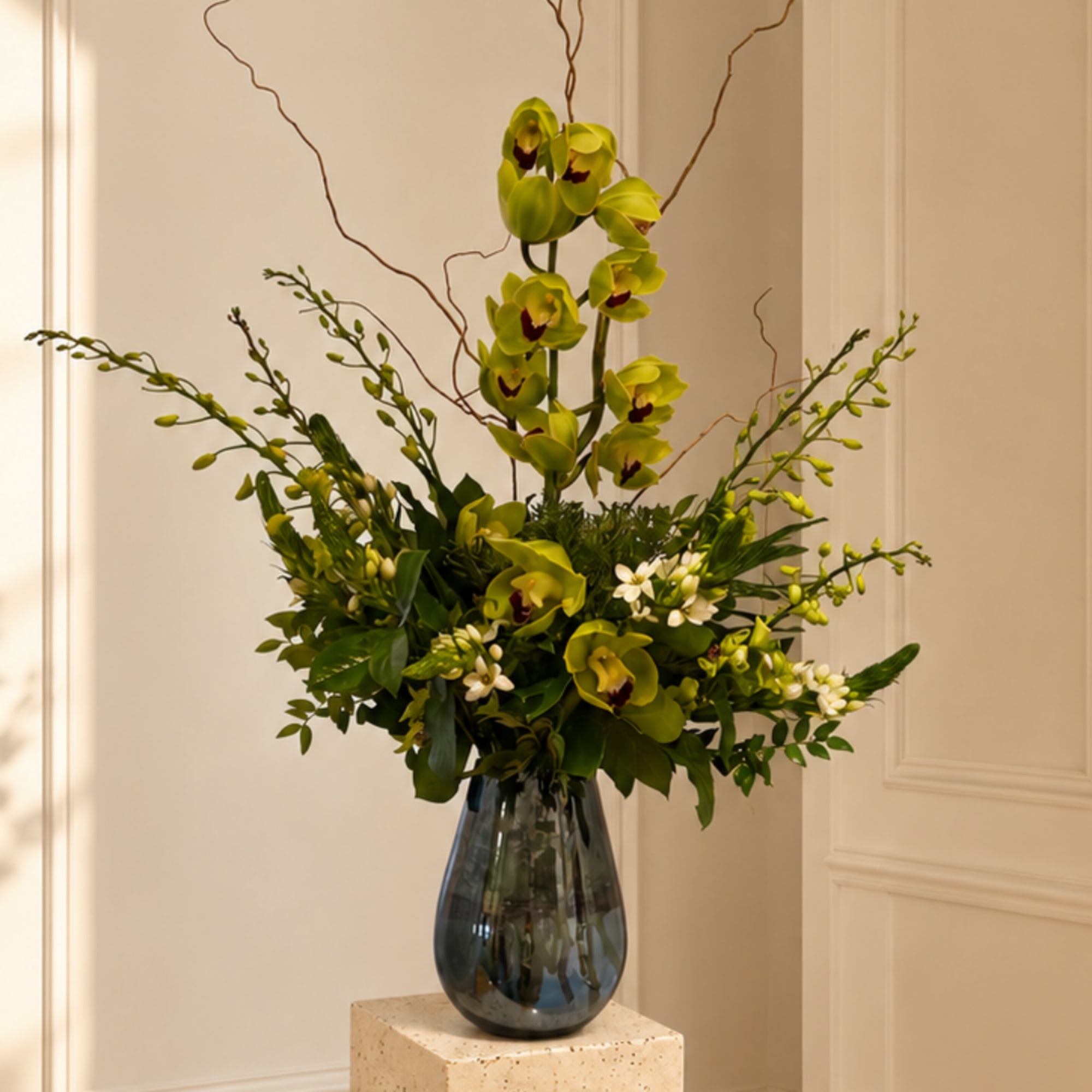 Green orchid arrangement in a dark glass vase