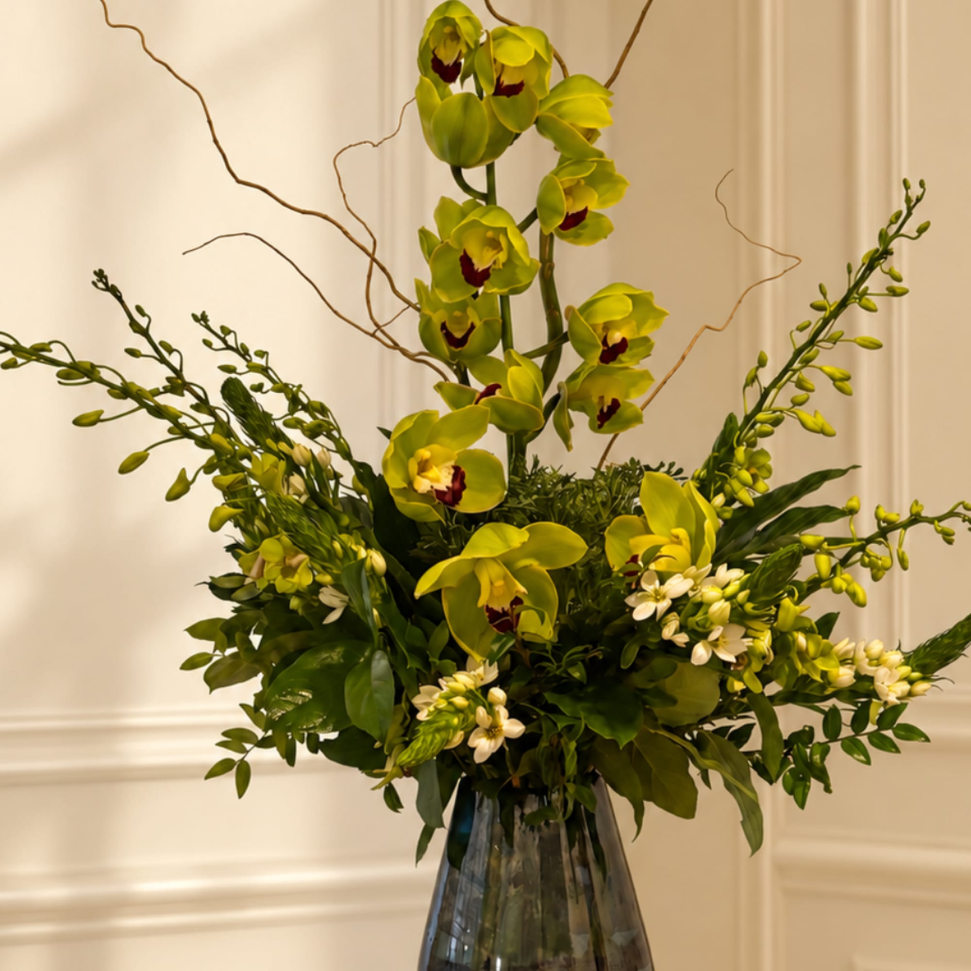 Tall green orchid arrangement in a glass vase with white accent flowers