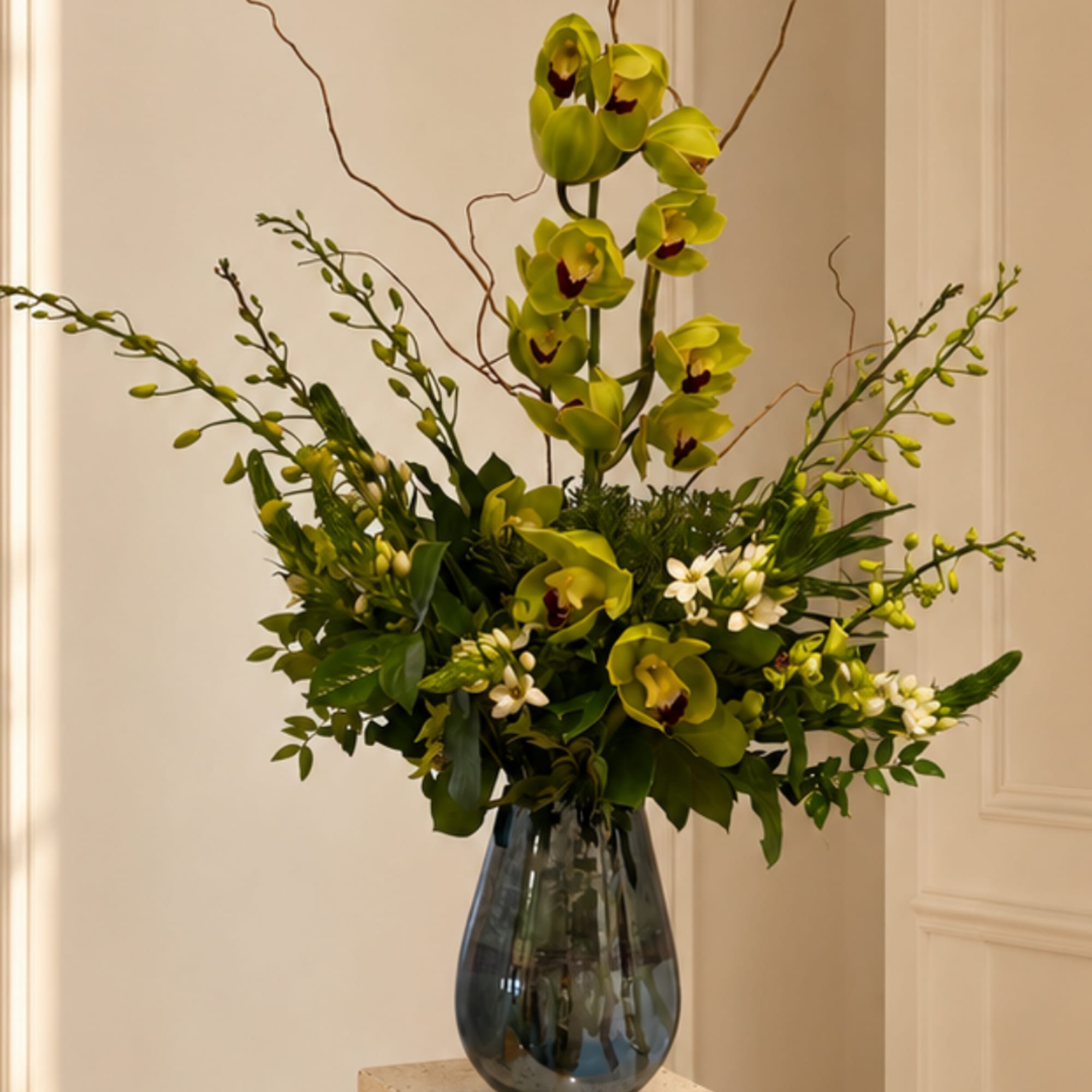 Tall green orchid arrangement in a dark glass vase