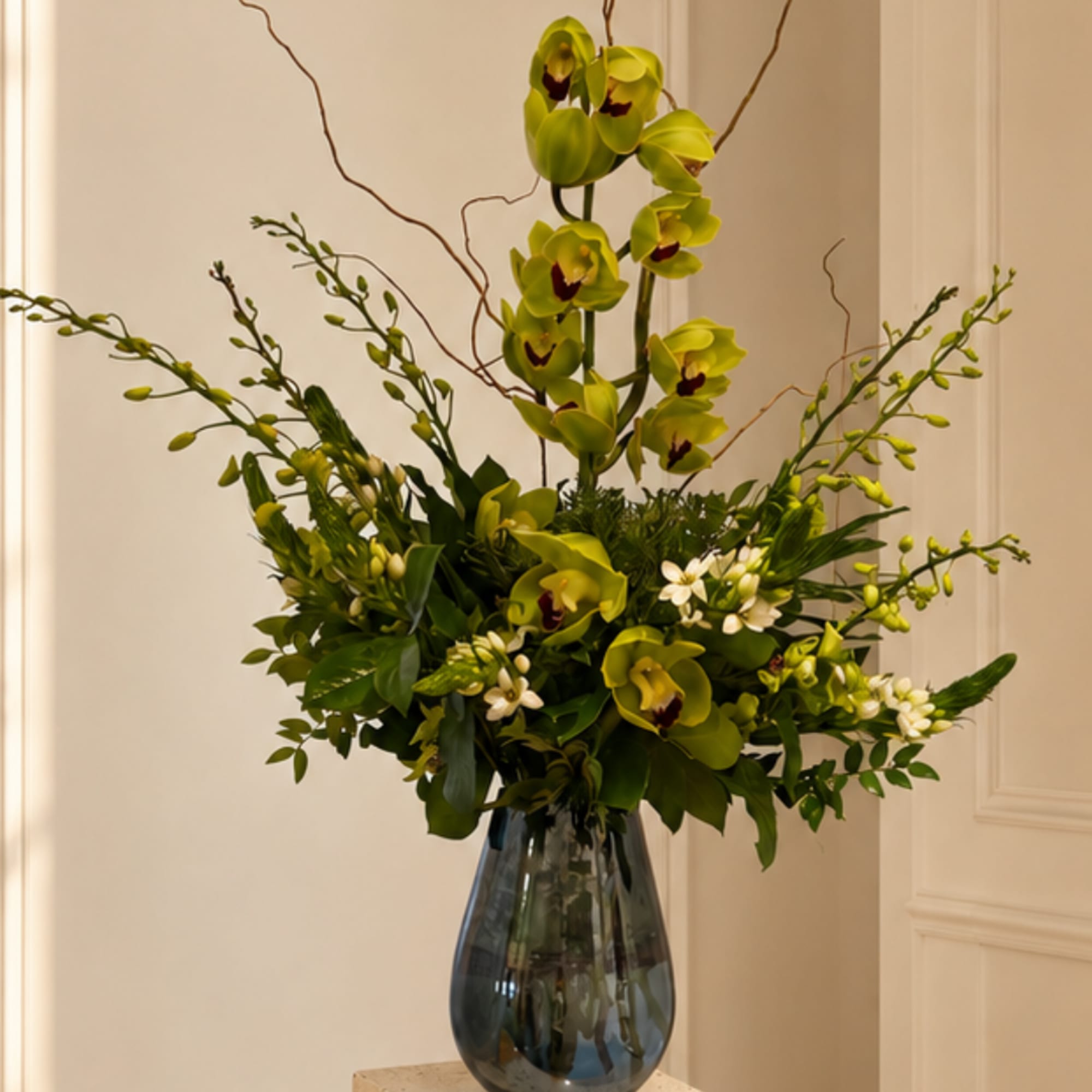 Green orchid arrangement in a dark glass vase