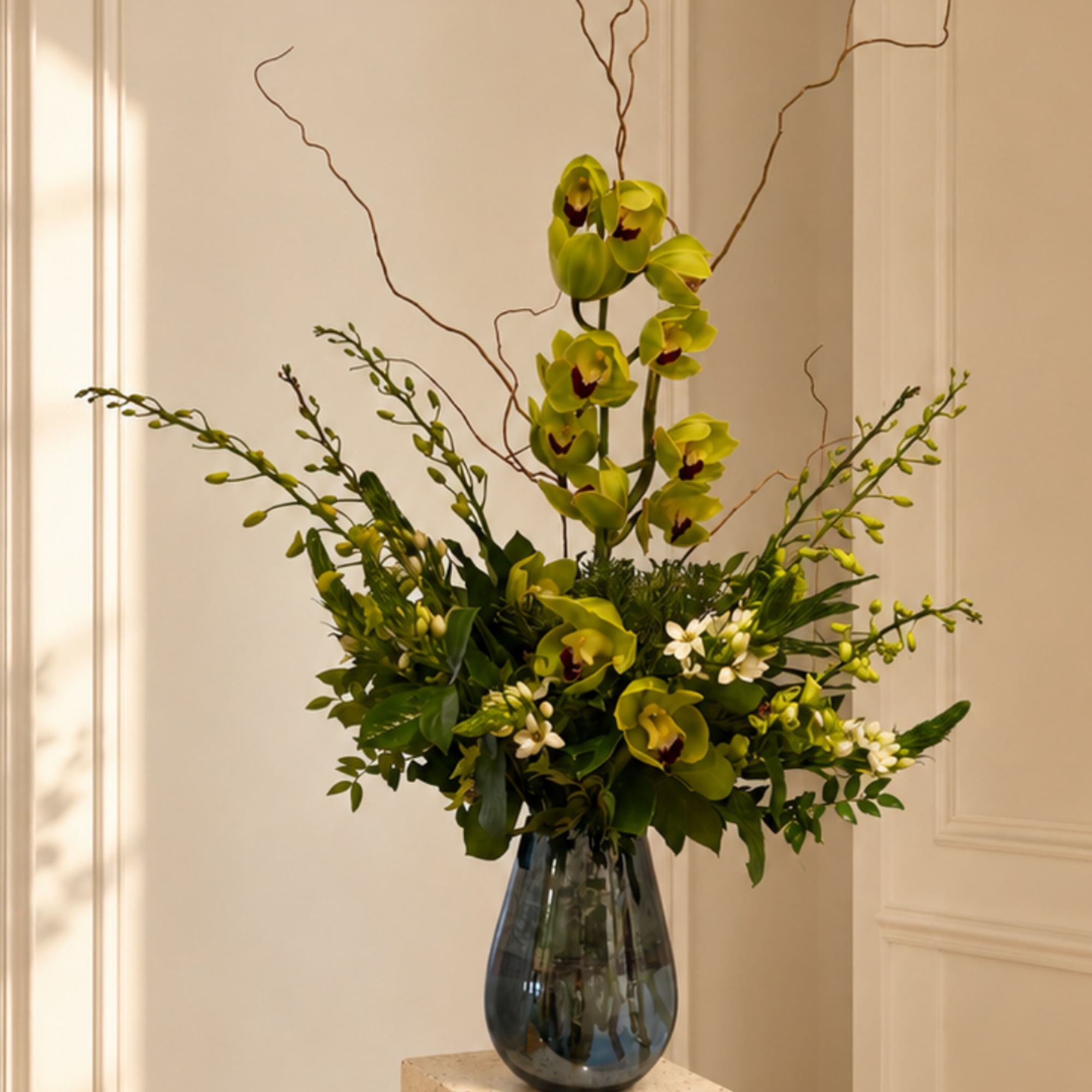 Tall green orchid arrangement in a dark glass vase