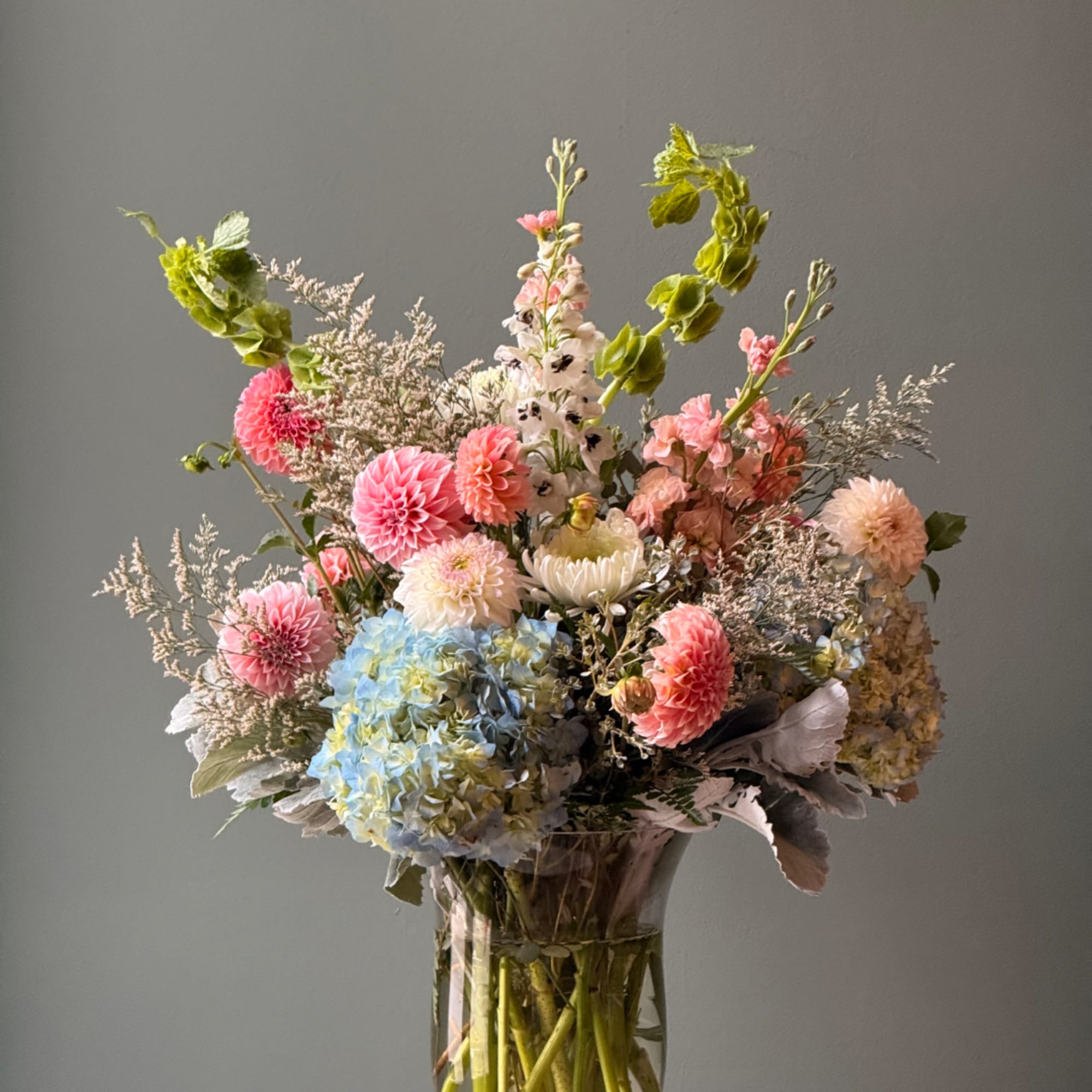 Mixed pastel bouquet in a clear glass vase with pink, blue, and white blooms
