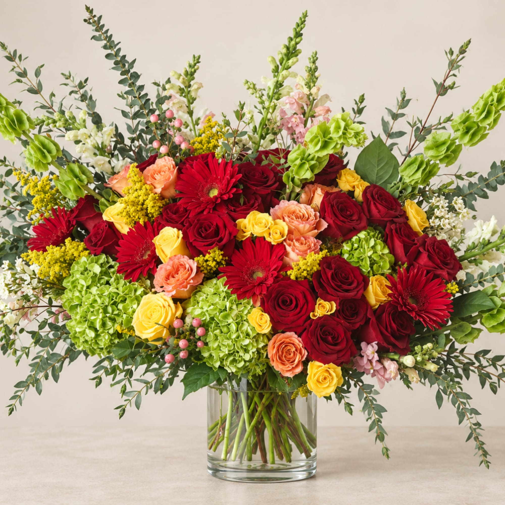 Large bouquet of red, yellow, and peach flowers in a glass vase