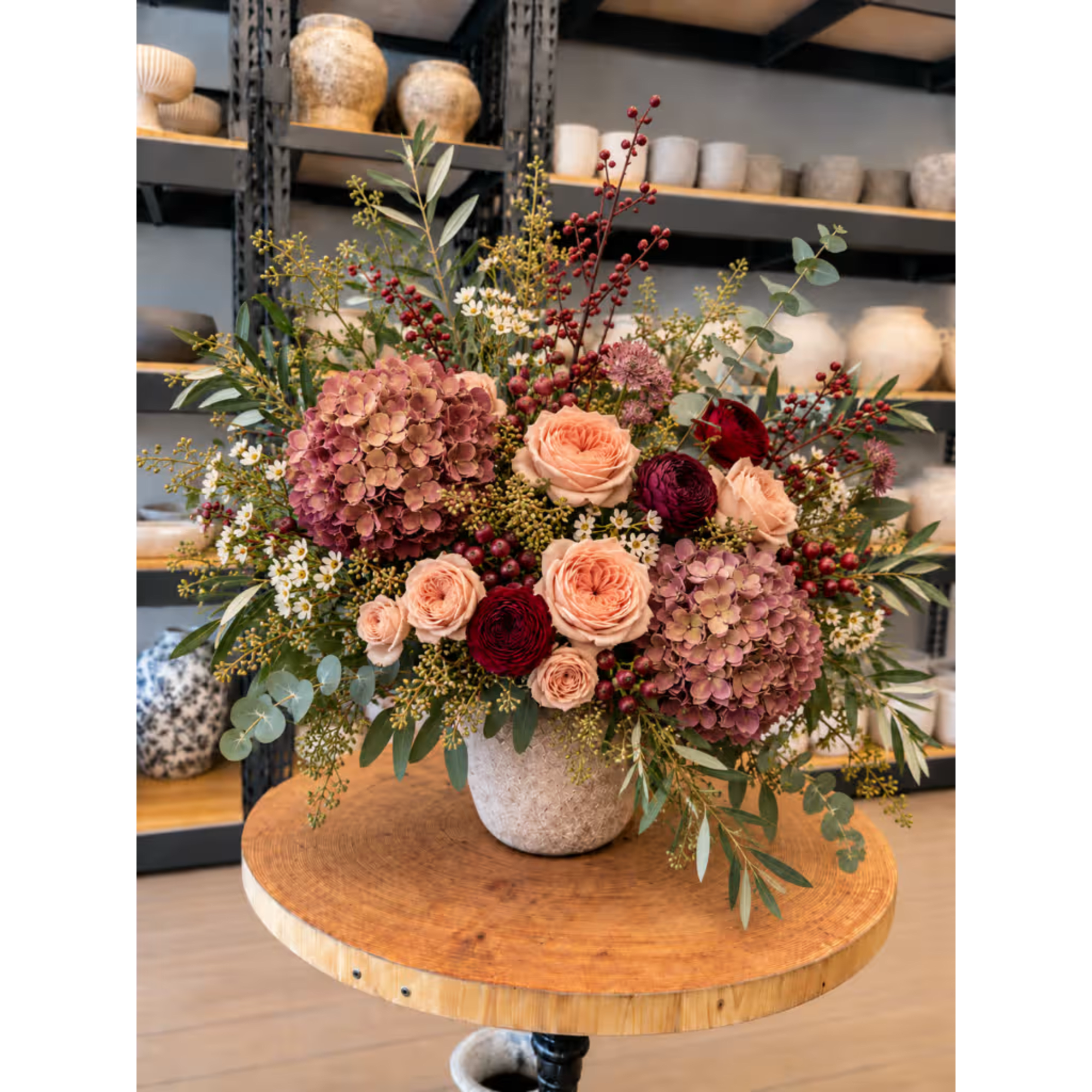 Mixed bouquet in a stone vase with roses, hydrangeas, and berries