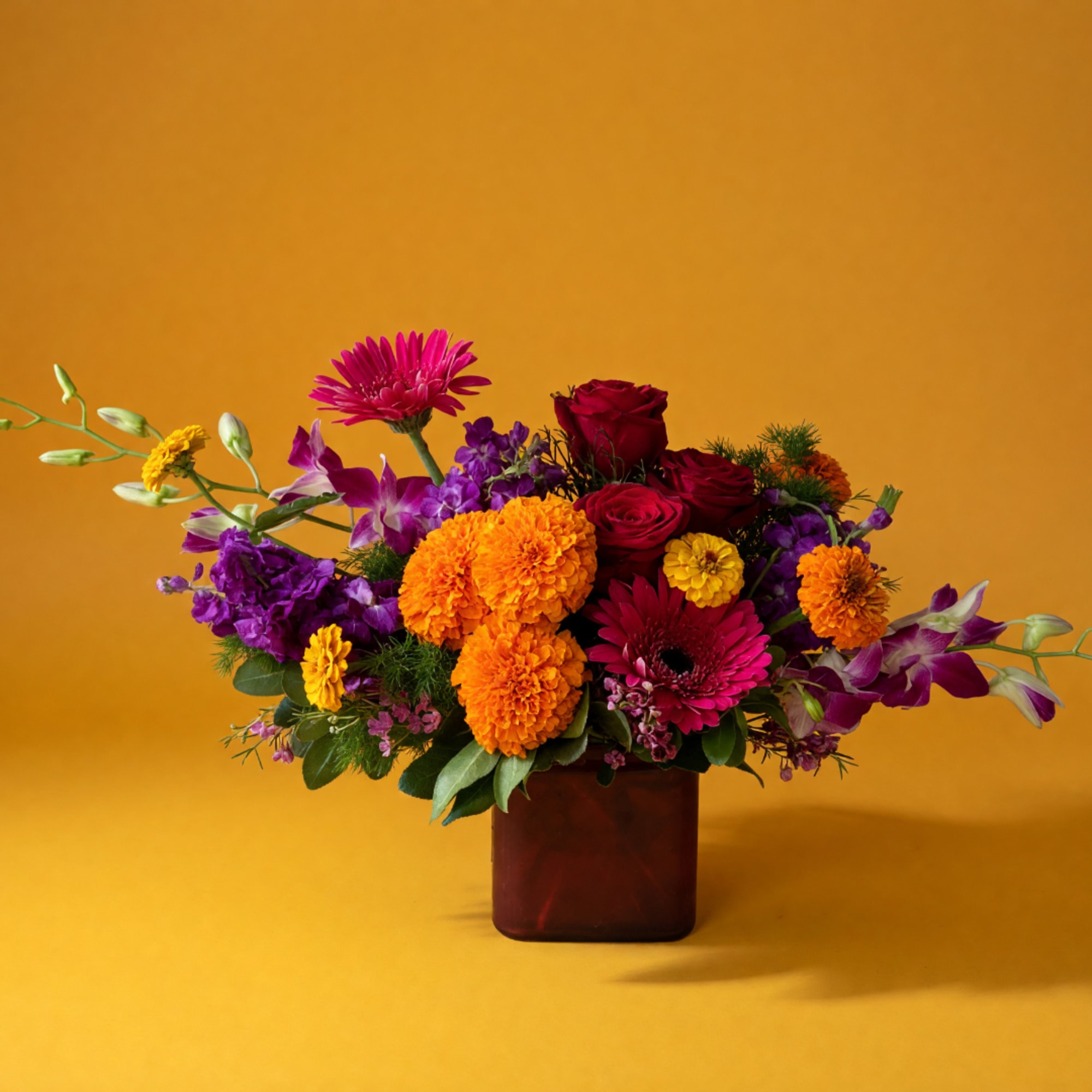 Colorful bouquet of roses, gerbera daisies, and marigolds in a square vase