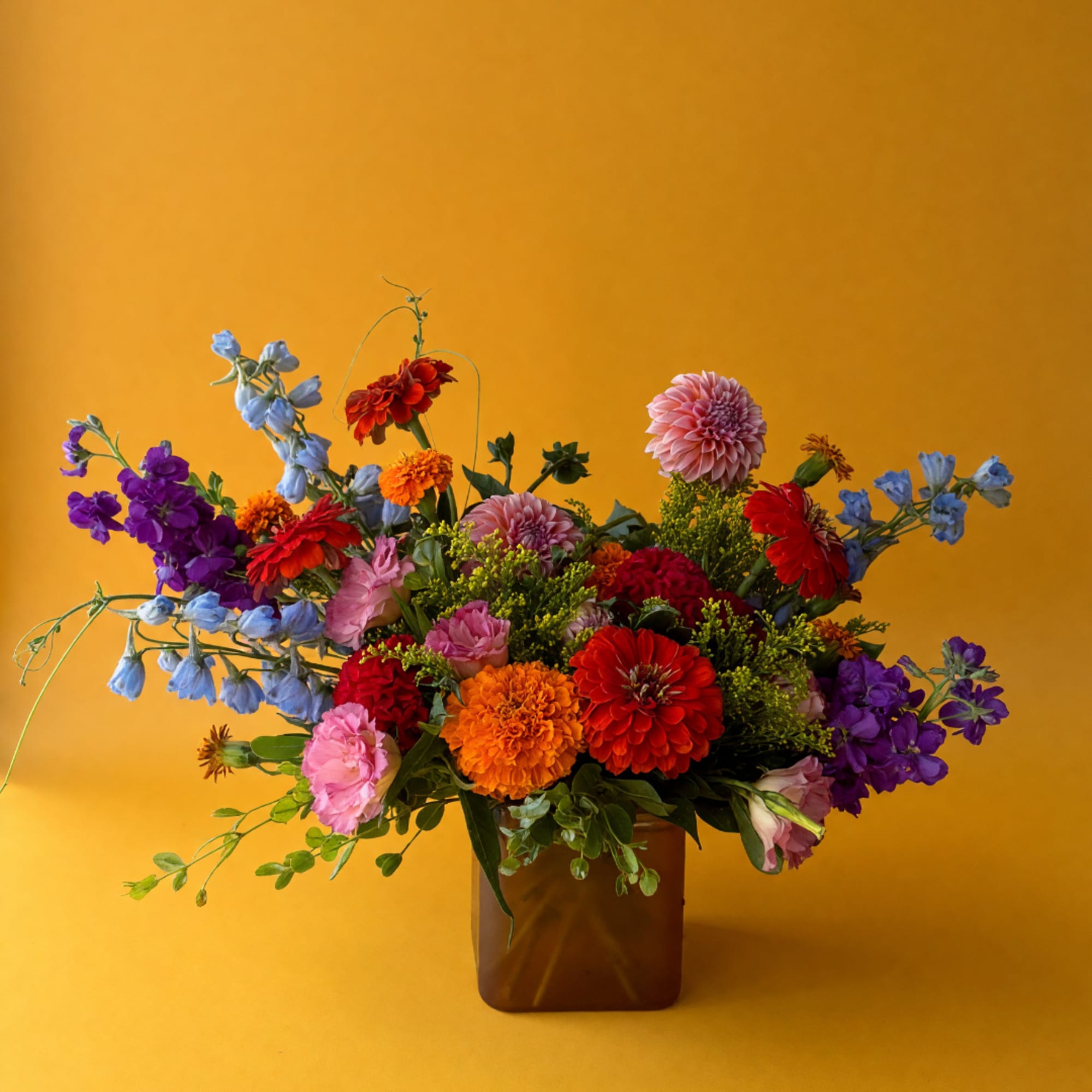 Colorful mixed bouquet in a brown vase against a yellow background