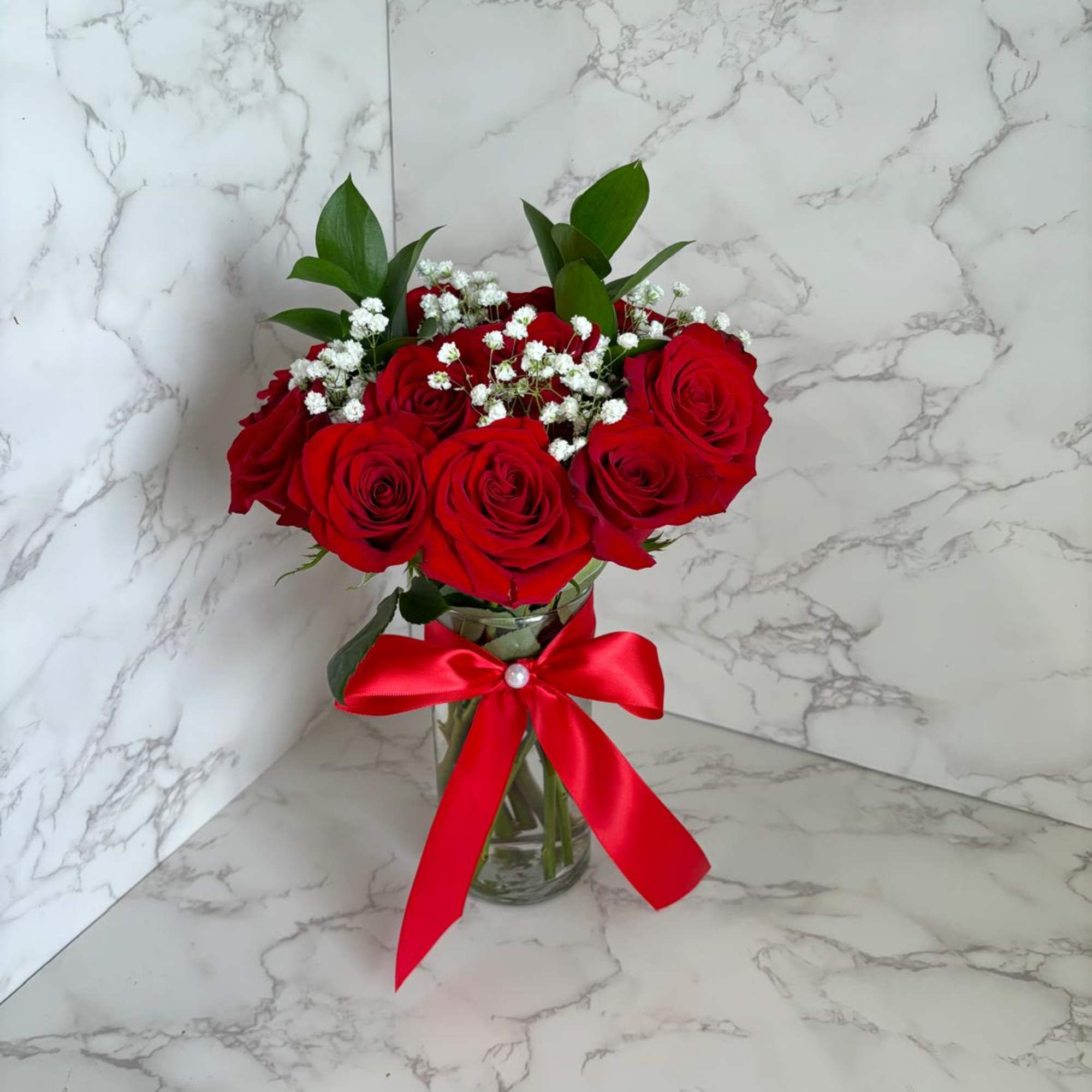 Red roses in a glass vase with baby's breath and a red ribbon
