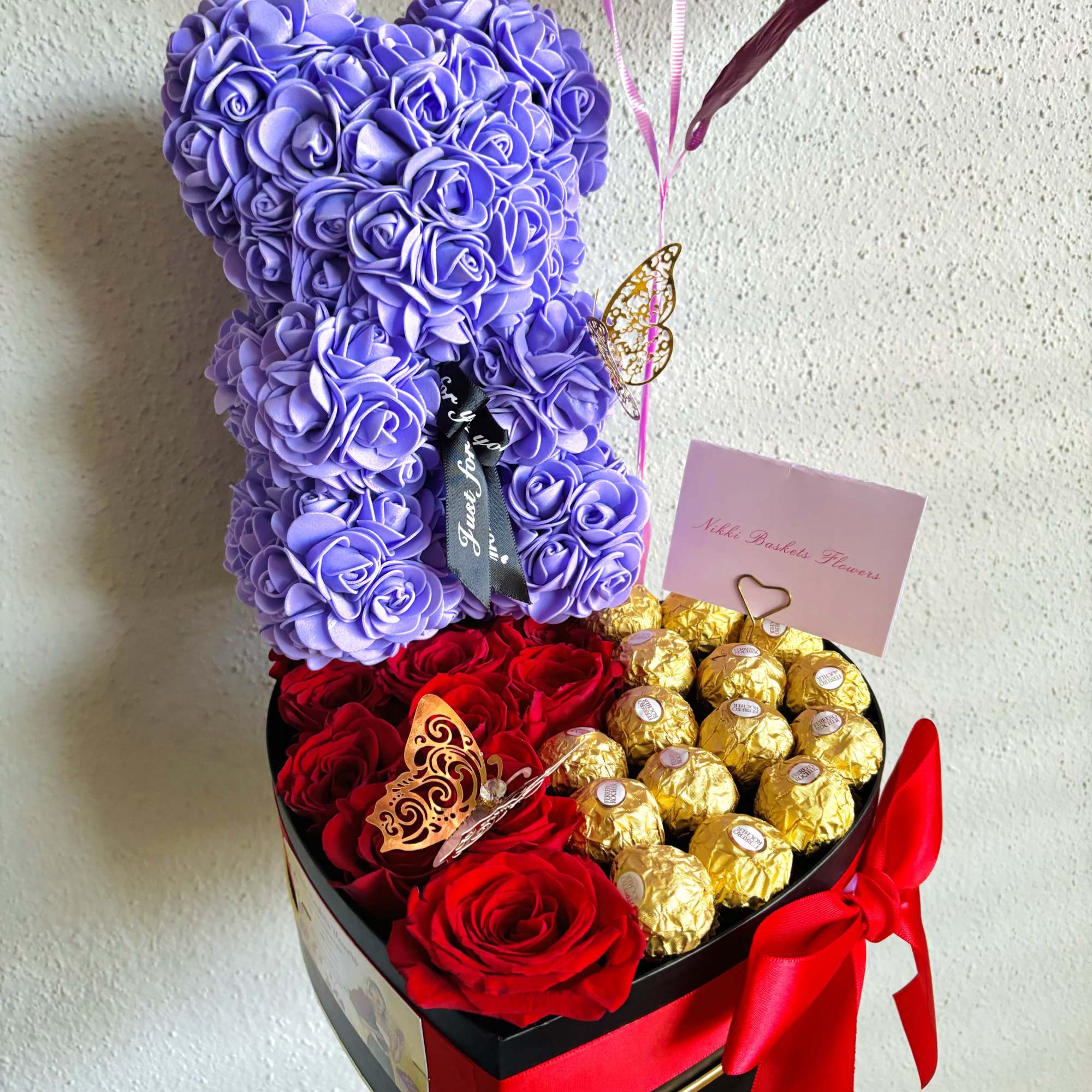Purple teddy bear made of roses above red roses and gold chocolates in a heart box
