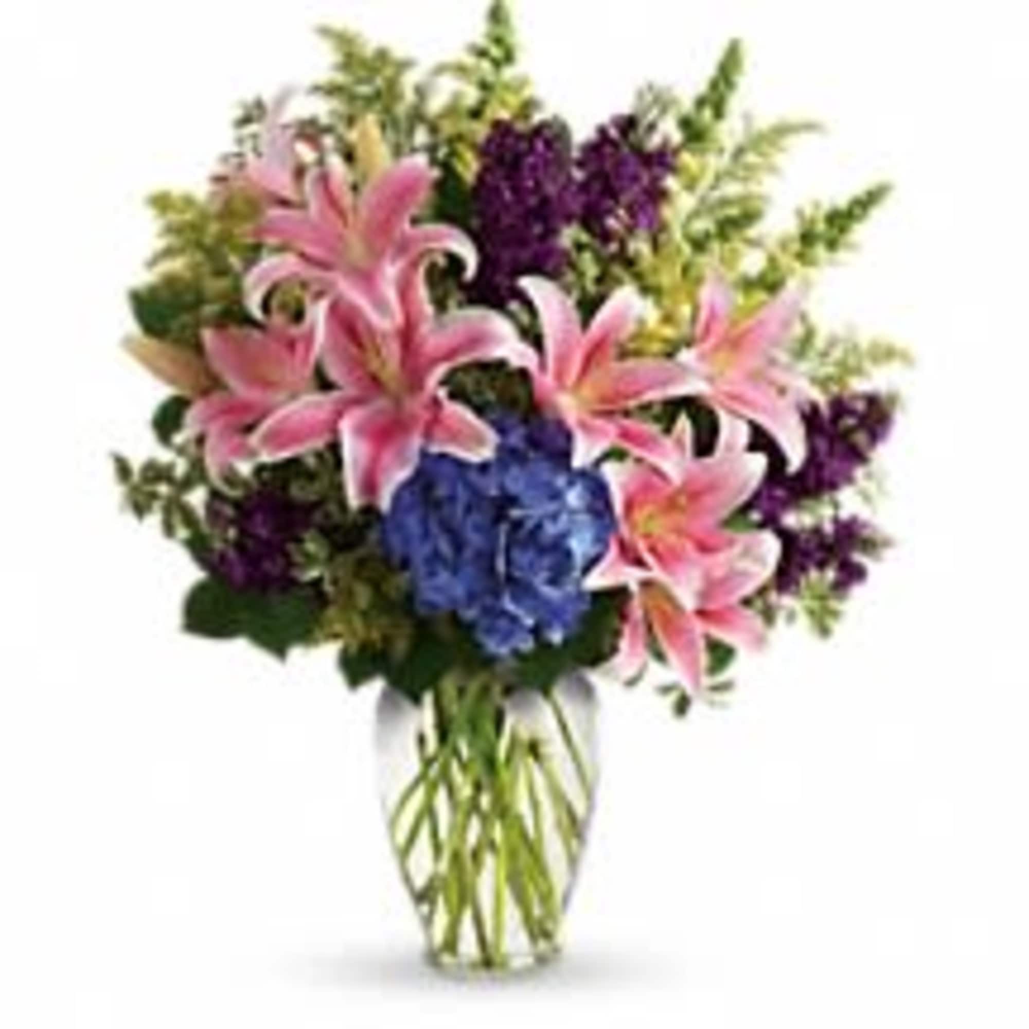 Bouquet of pink lilies, blue hydrangea, and purple flowers in a glass vase