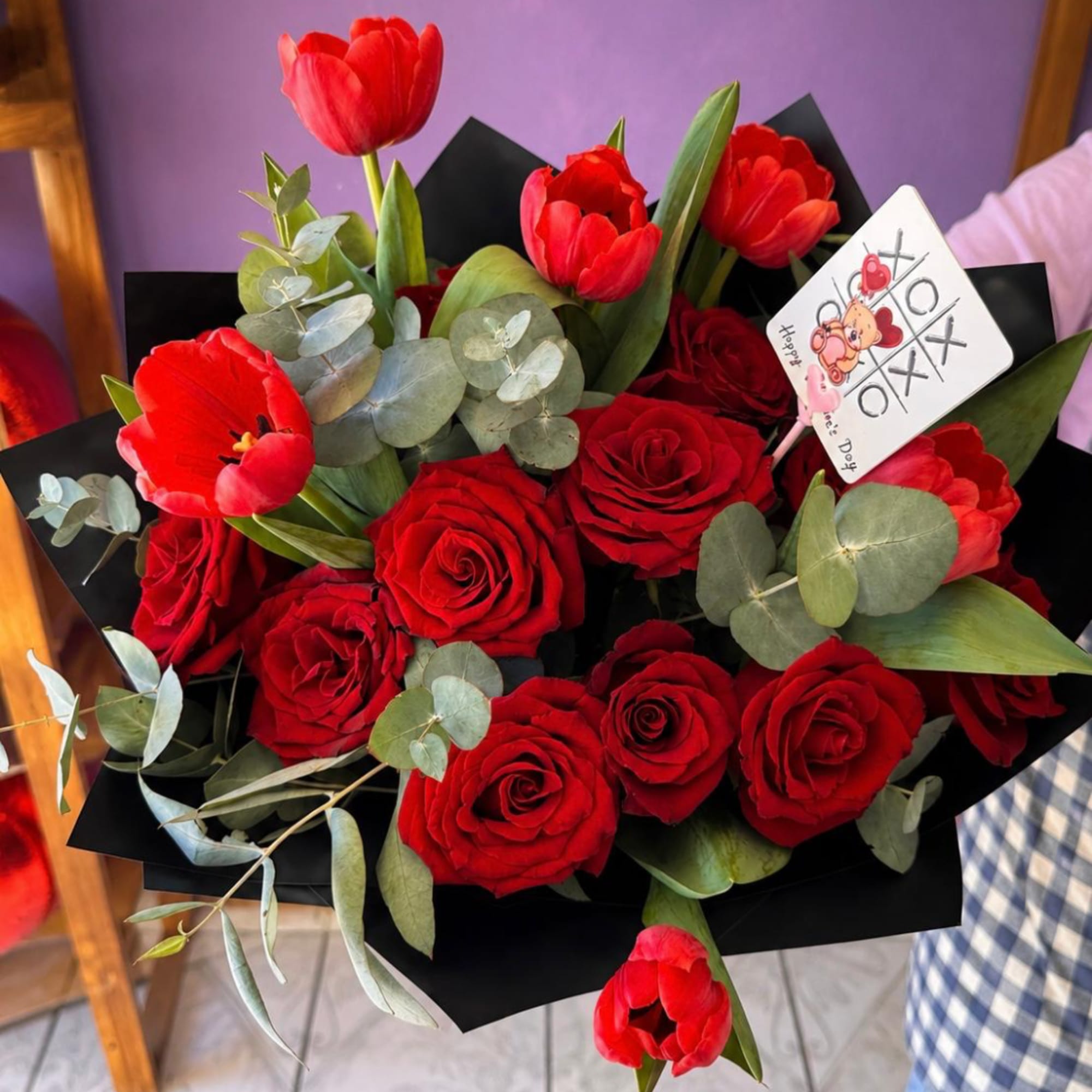 Bouquet of red roses and red tulips with eucalyptus in black wrap
