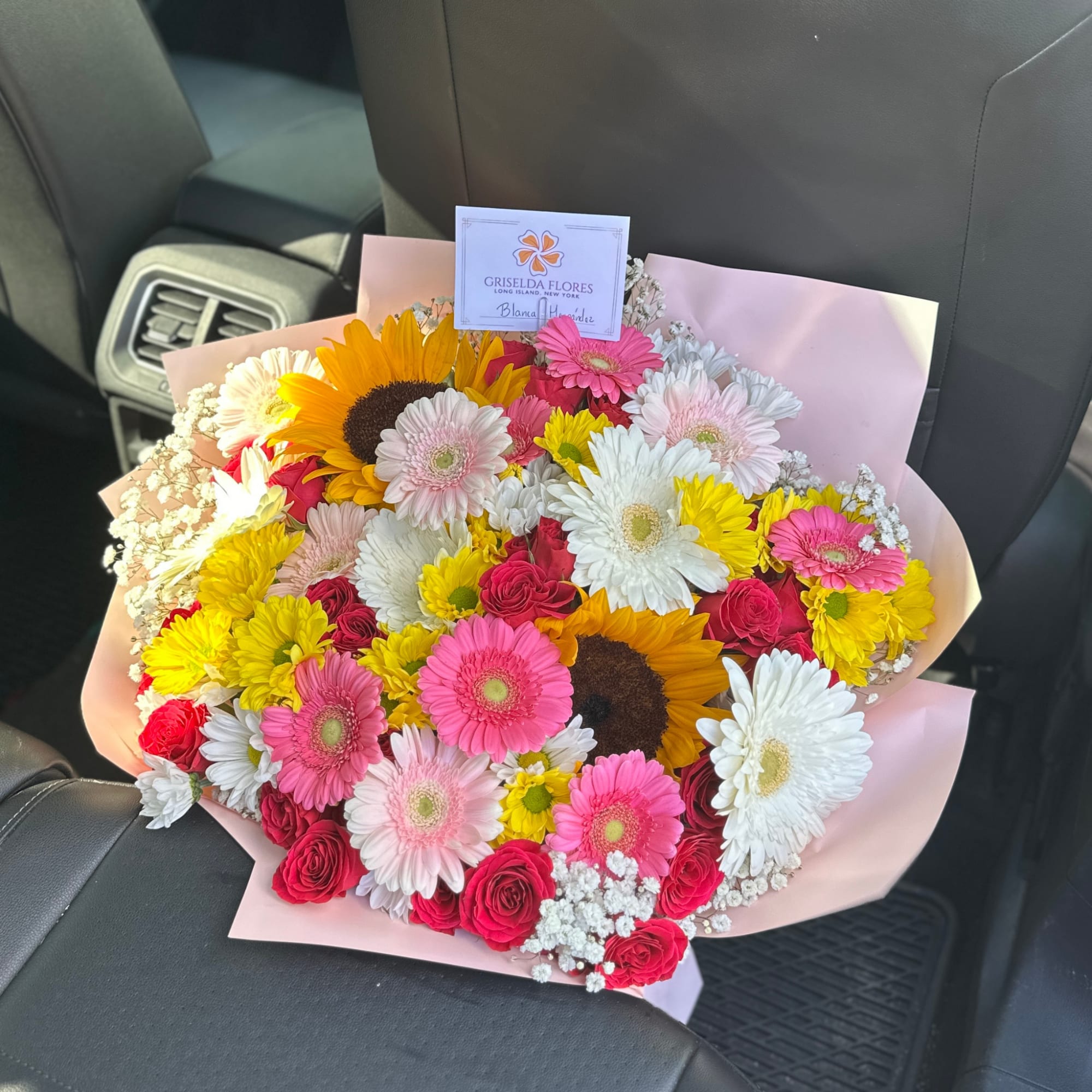 Mixed bouquet of gerbera daisies, sunflowers, and roses wrapped in pink paper