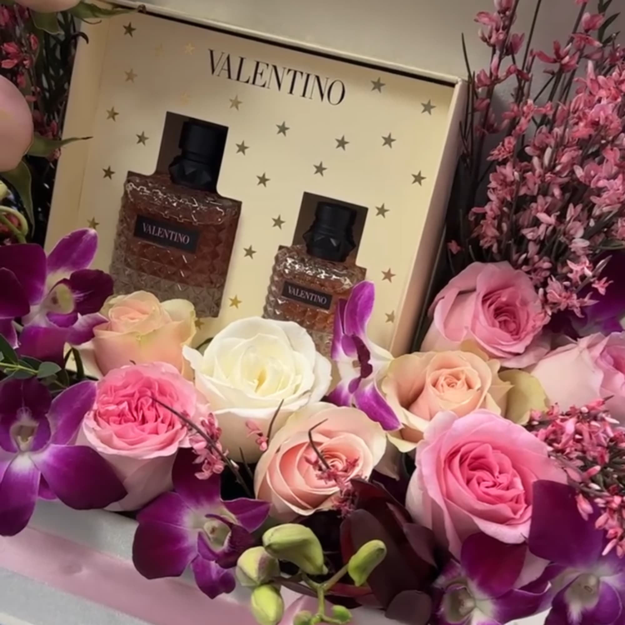 Pink and white roses with purple orchids around a Valentino gift set