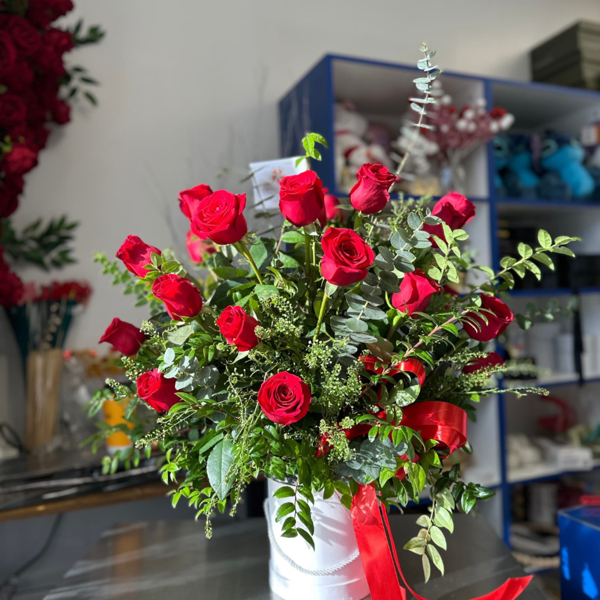 Red roses arranged in a white hatbox with a red ribbon.