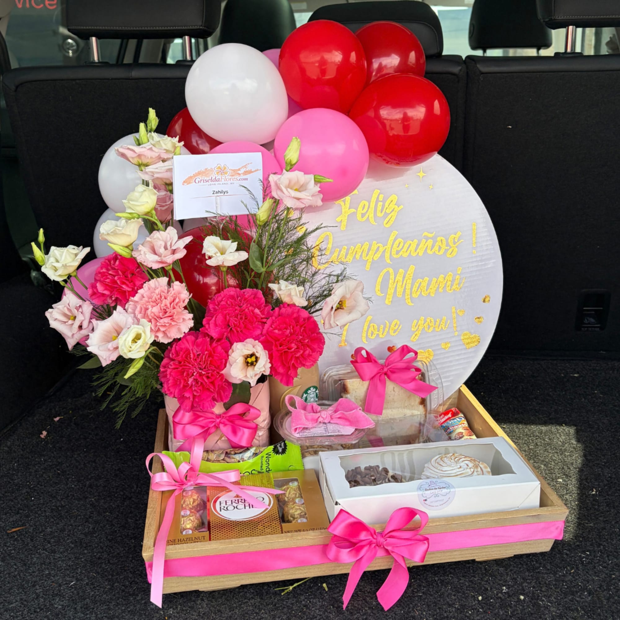 Birthday gift arrangement with pink flowers, balloons, and chocolates in a wooden tray