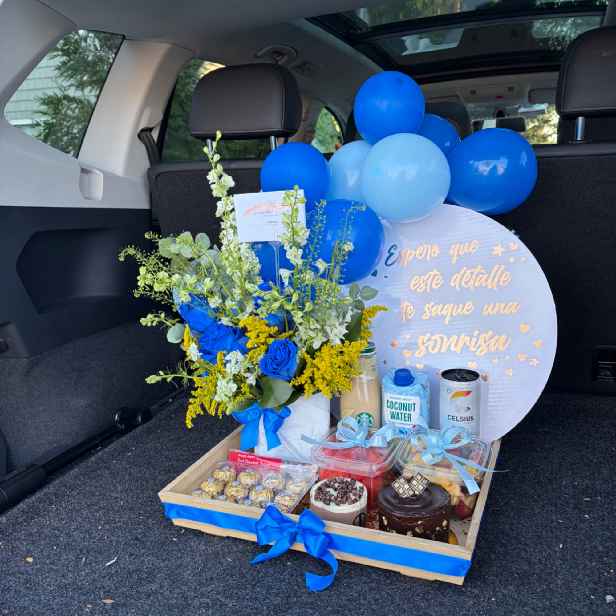 Blue flower arrangement with balloons and a gift tray in a car trunk