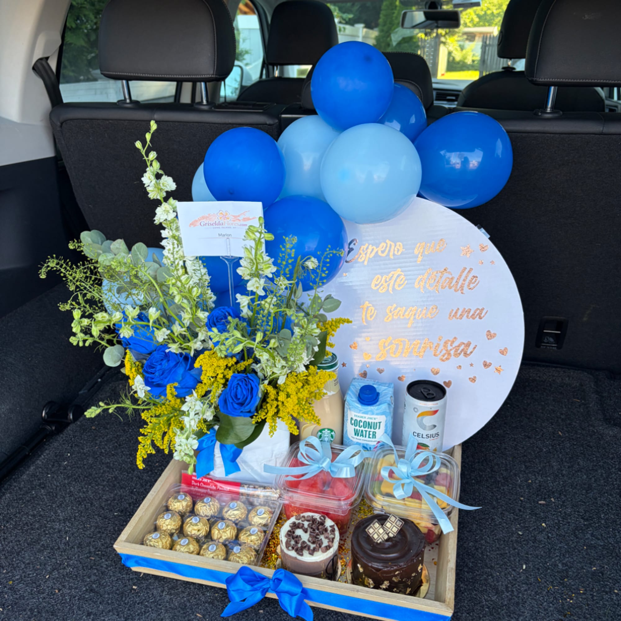 Blue balloons with a flower arrangement, chocolates, and desserts in a gift tray