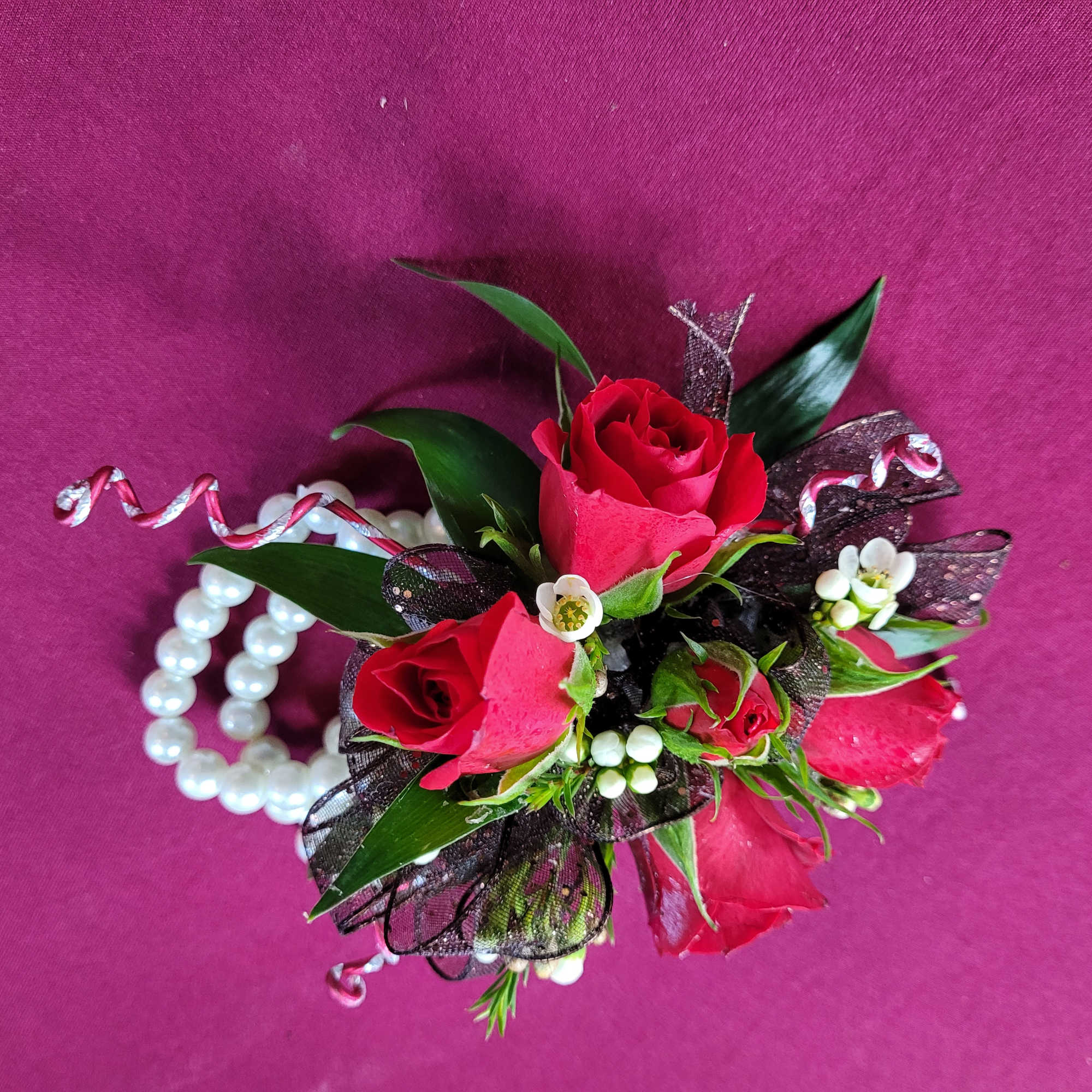 Small red rose corsage with pearl bracelet and ribbon on pink background