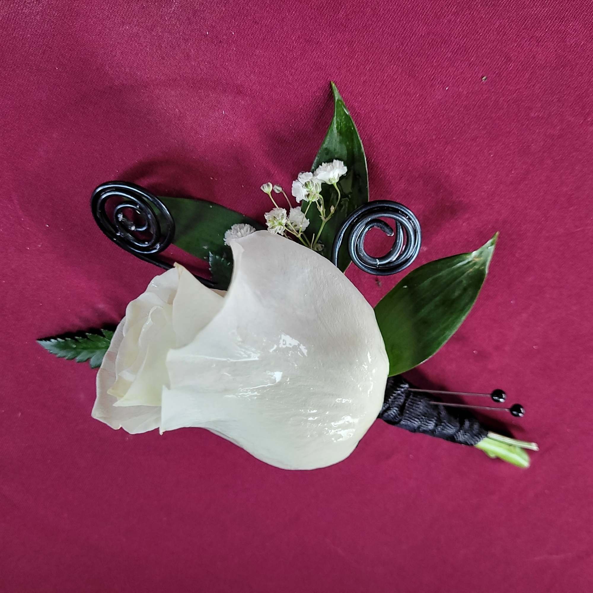 White calla lily boutonniere with dark green leaves on a magenta background