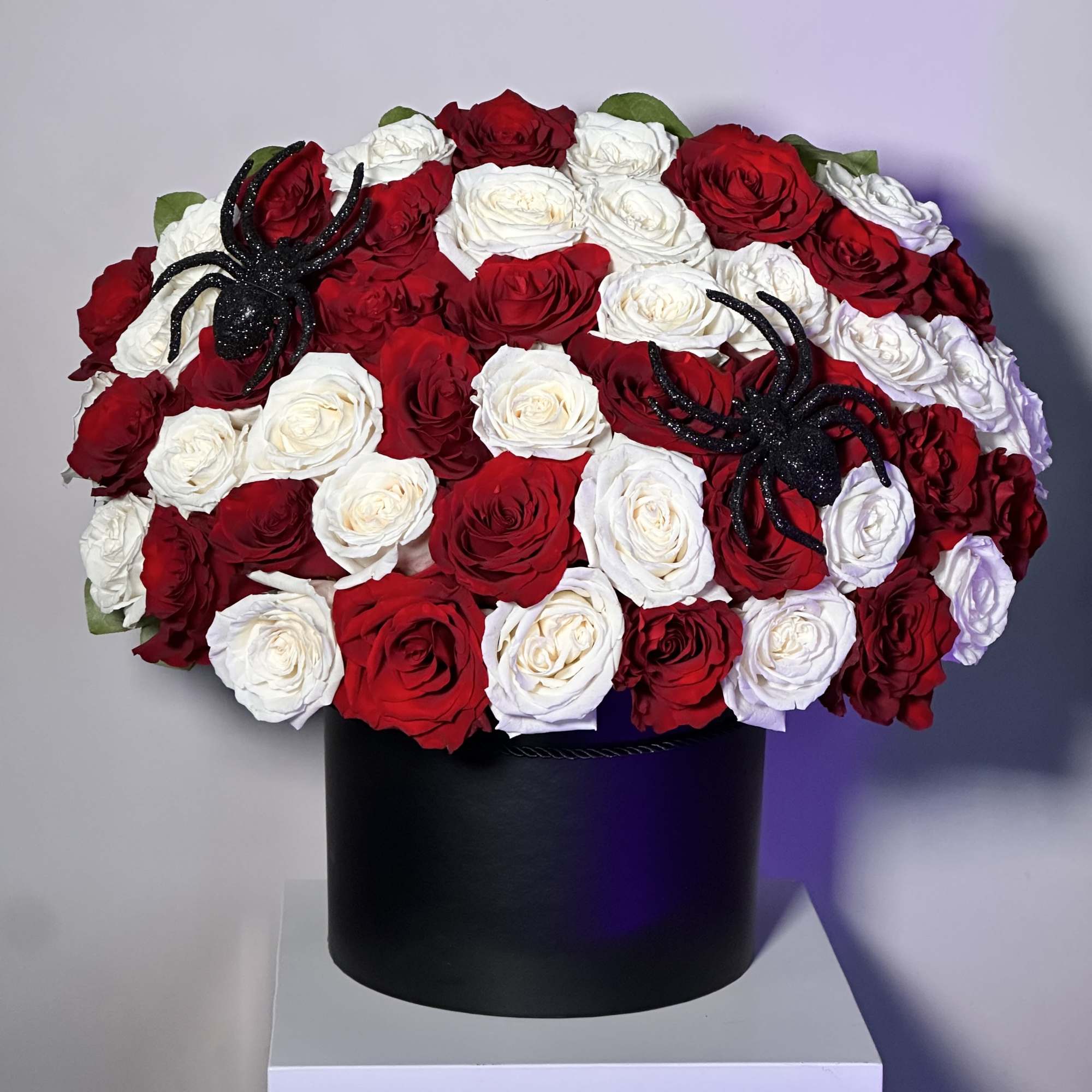 Round hat box arrangement of red and white roses with black glitter spiders.