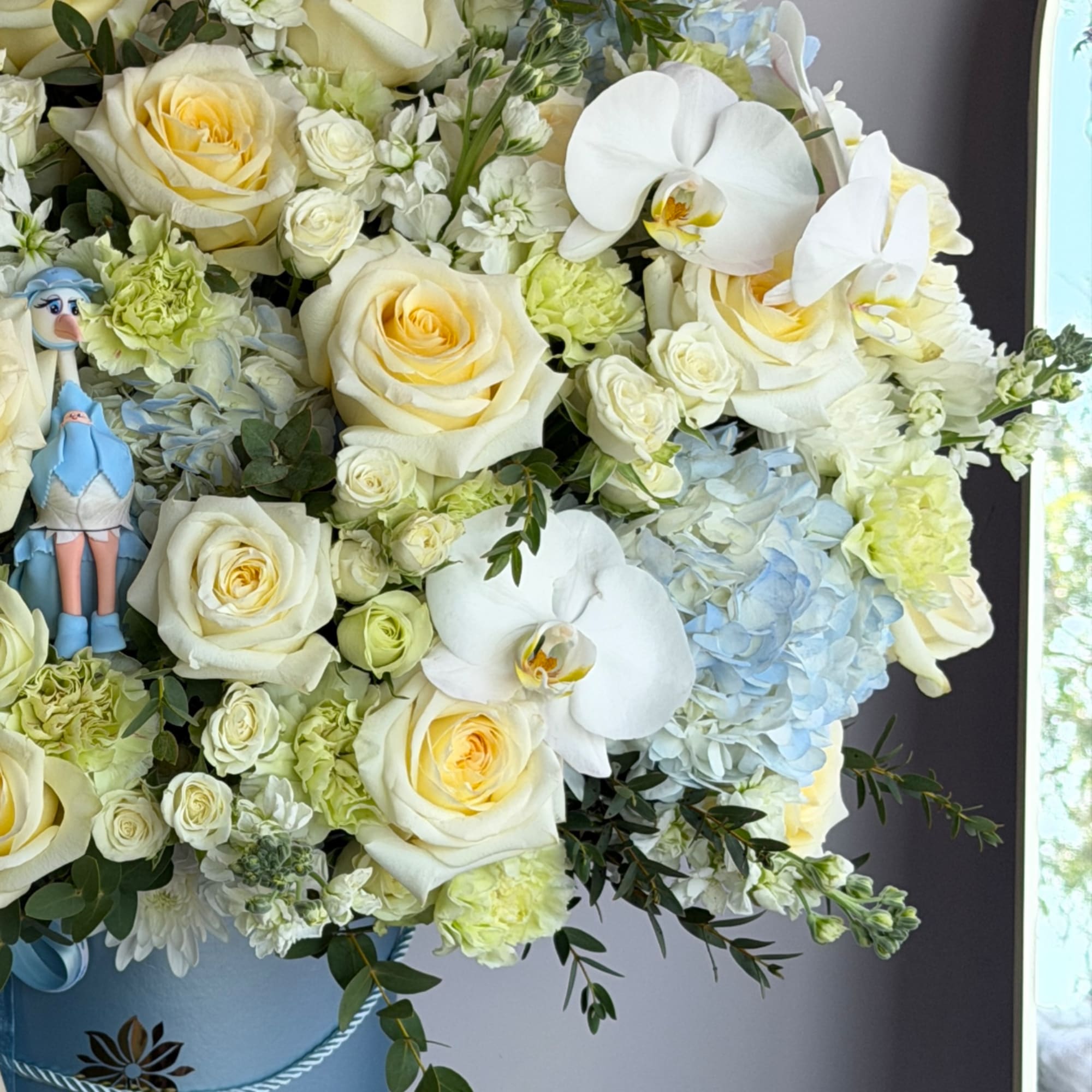 White and pale yellow roses with orchids and hydrangeas in a blue container.