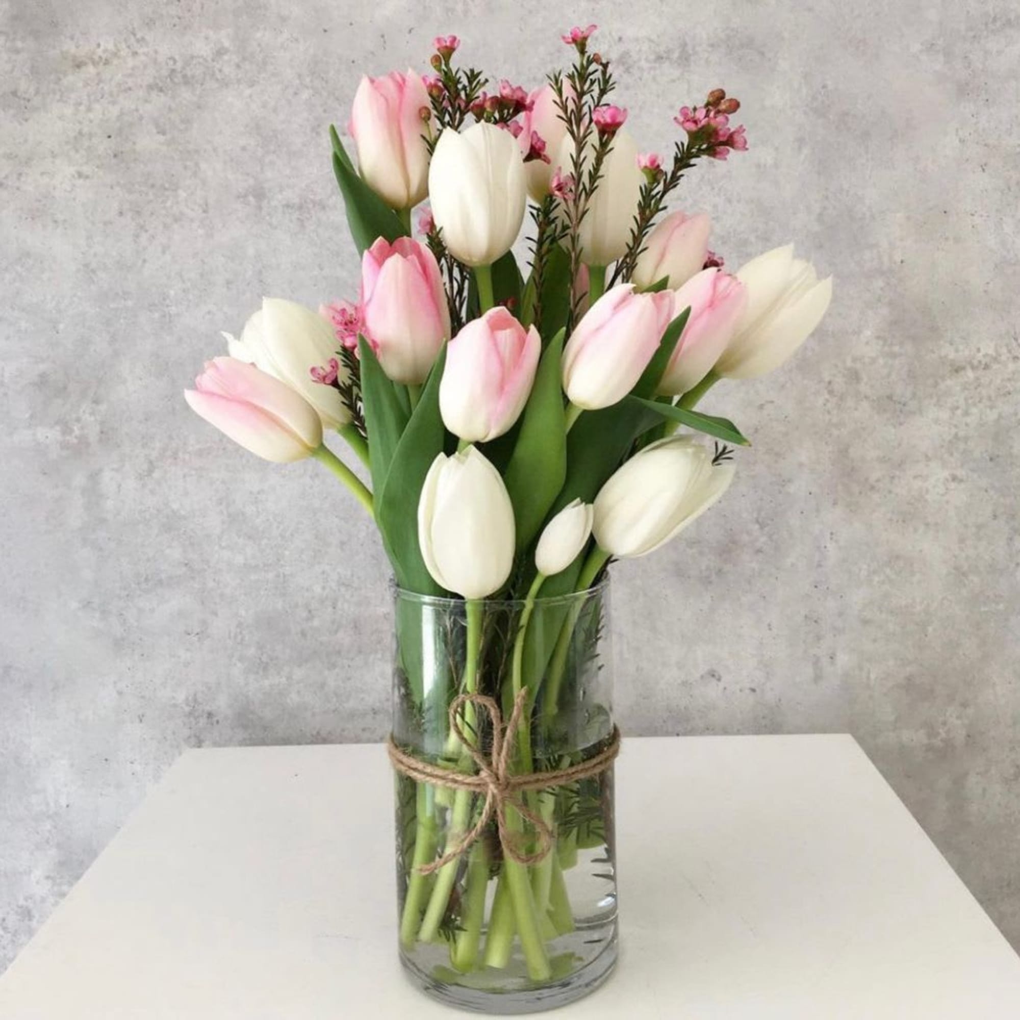Pink and white tulips in a clear glass vase tied with twine
