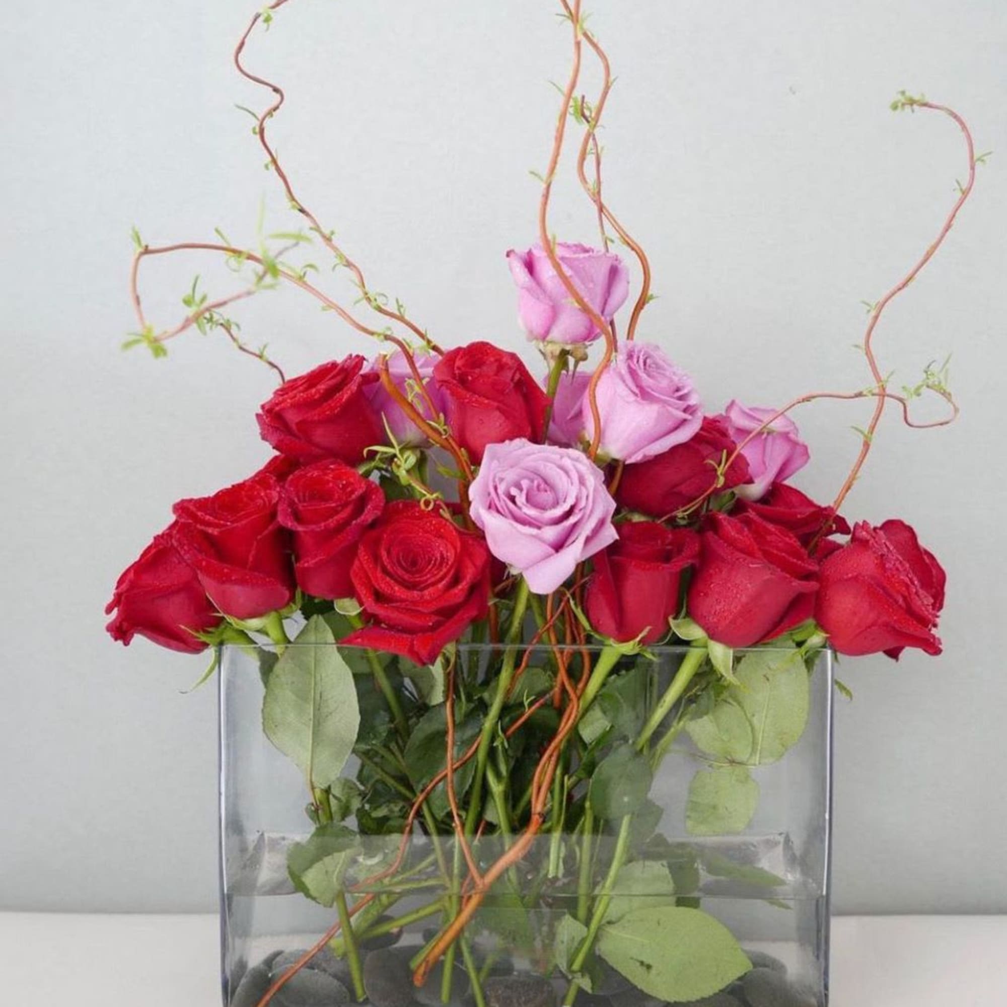 Red and pink roses arranged in a clear rectangular vase