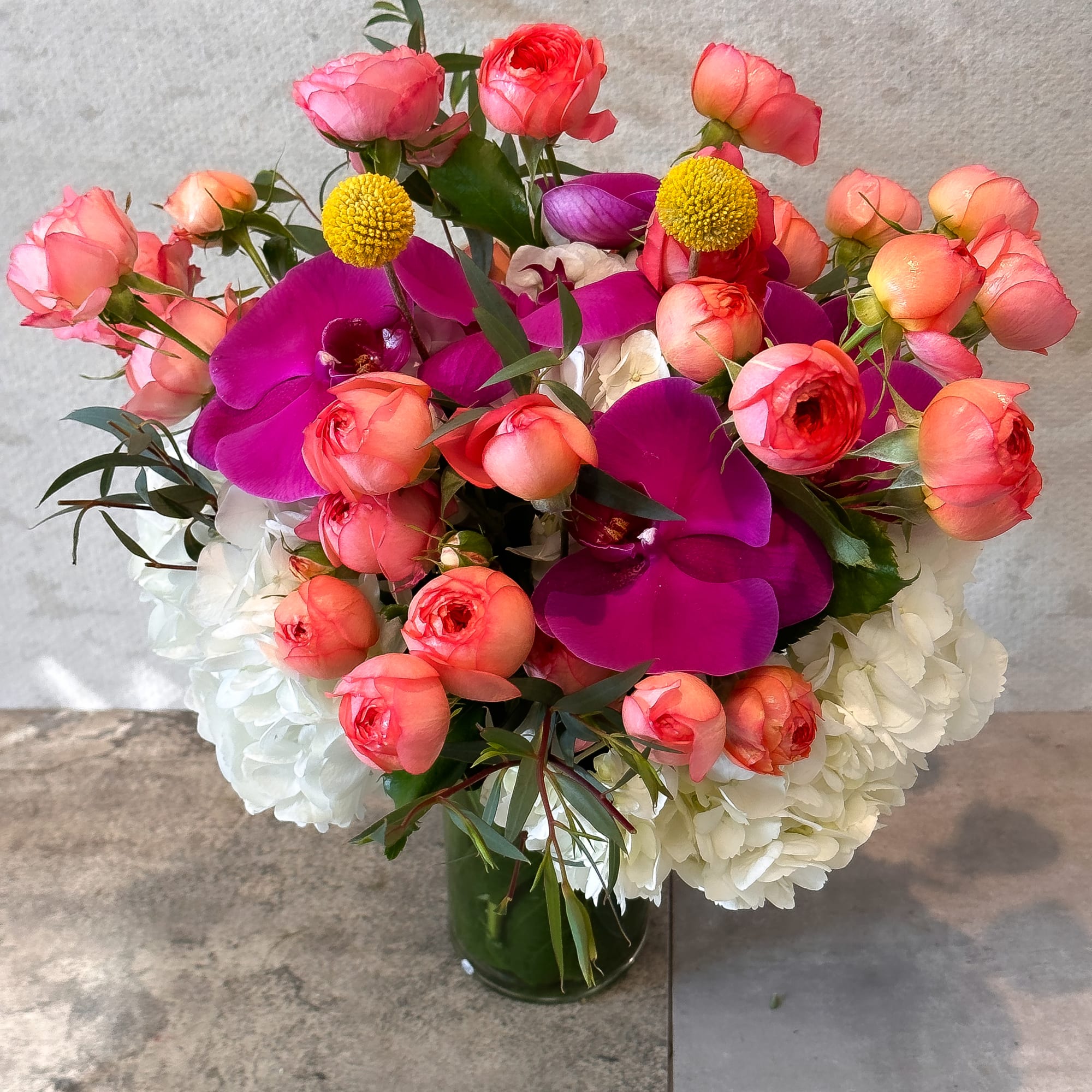 Bouquet of pink ranunculus, purple orchids, and white hydrangeas in a glass vase