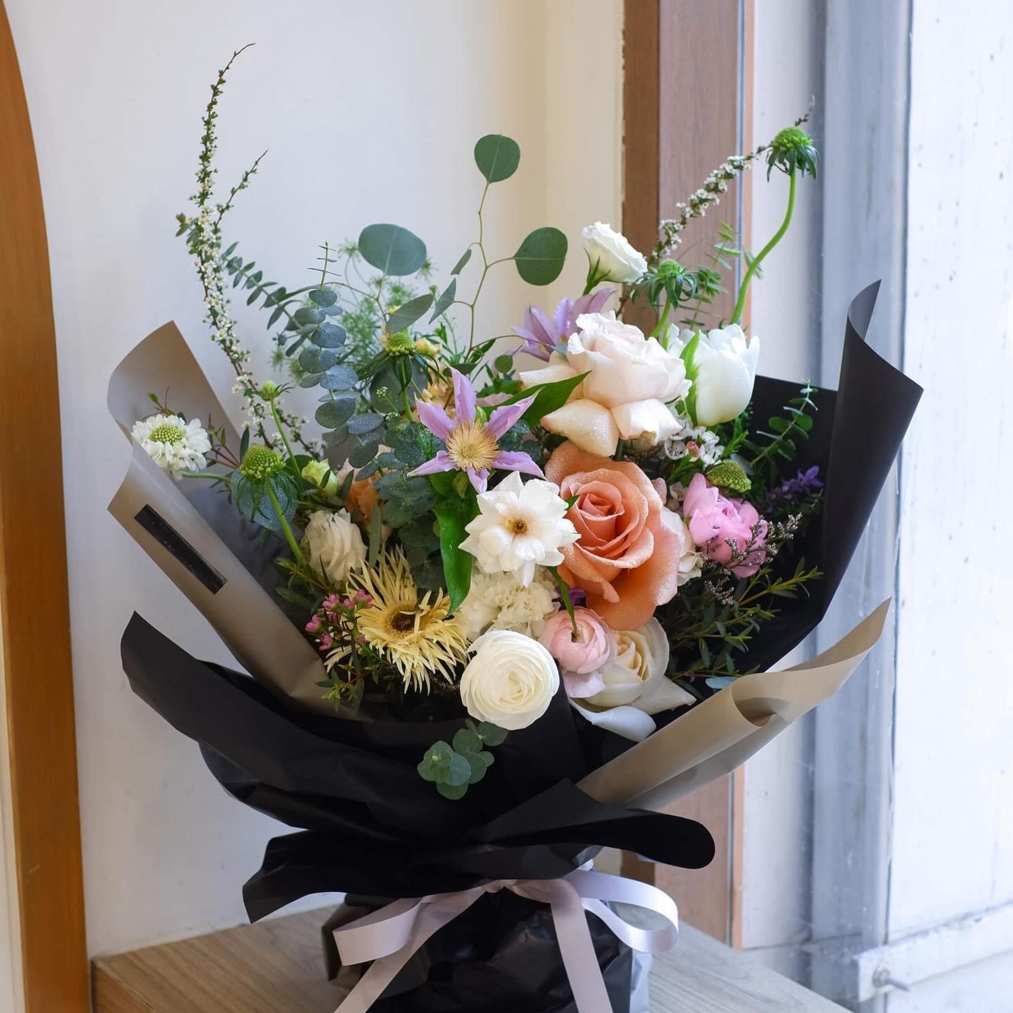 Mixed bouquet of pastel flowers wrapped in black paper with a ribbon