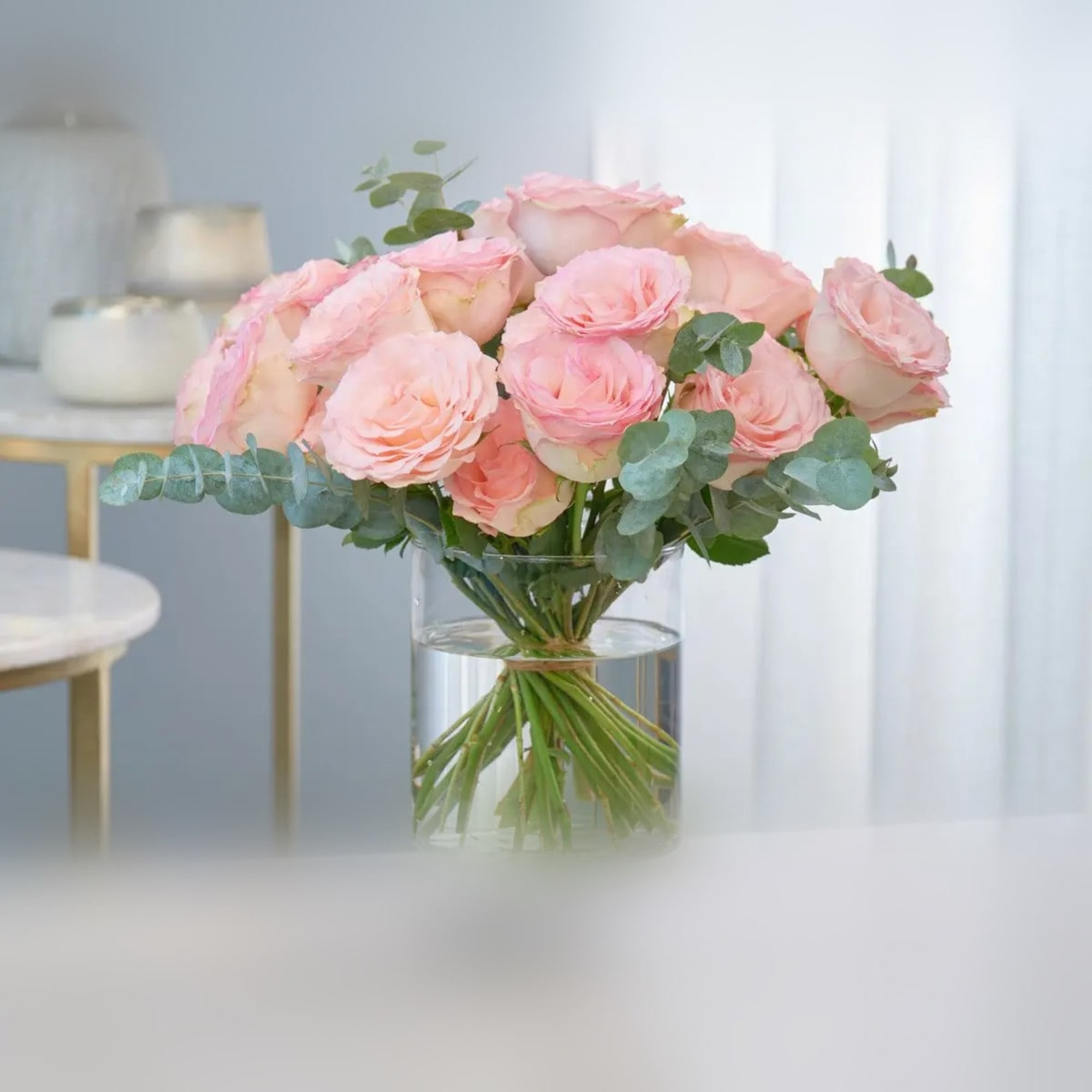 Pink roses arranged in a clear glass vase with eucalyptus