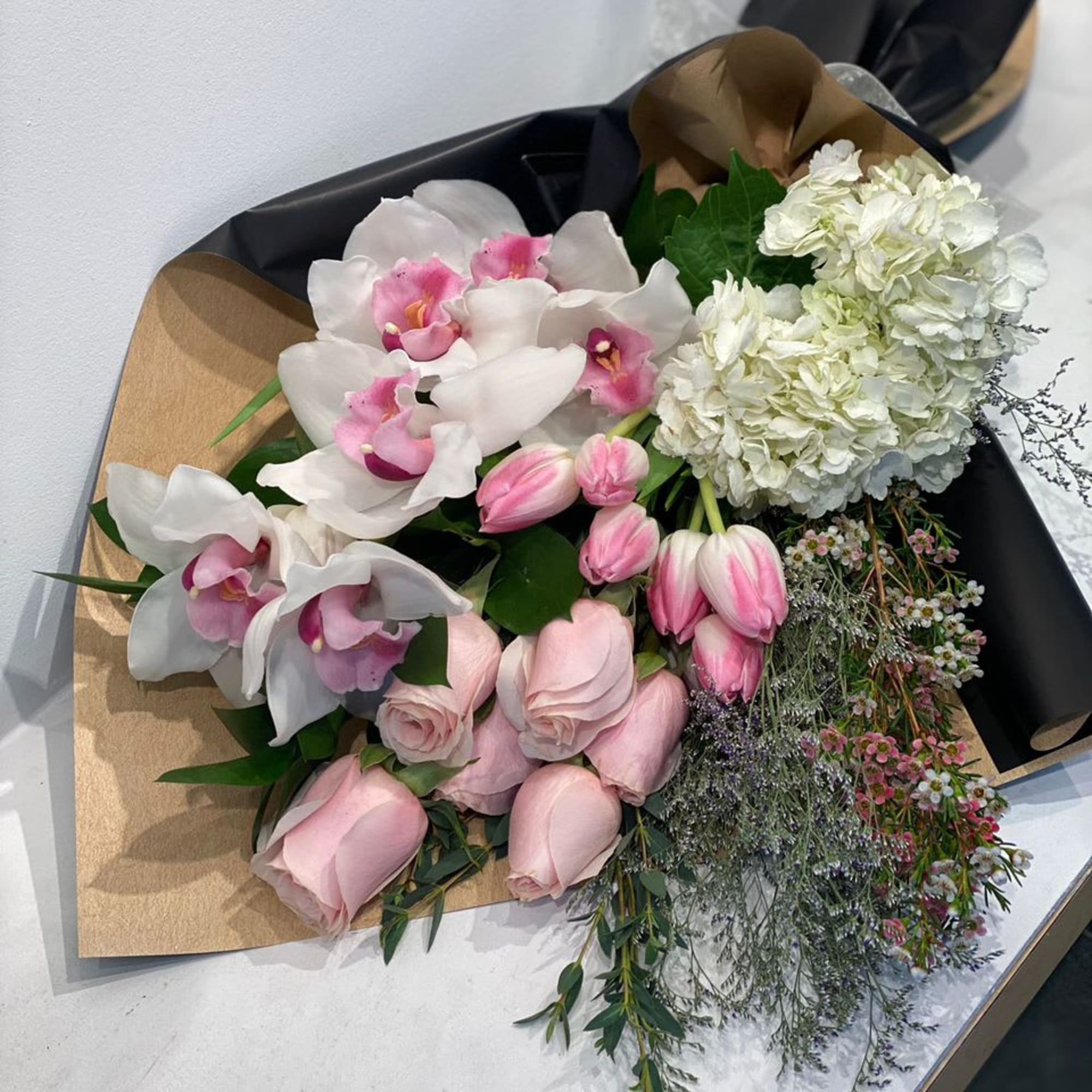 Bouquets of pink roses, white orchids, and white hydrangeas wrapped in black paper