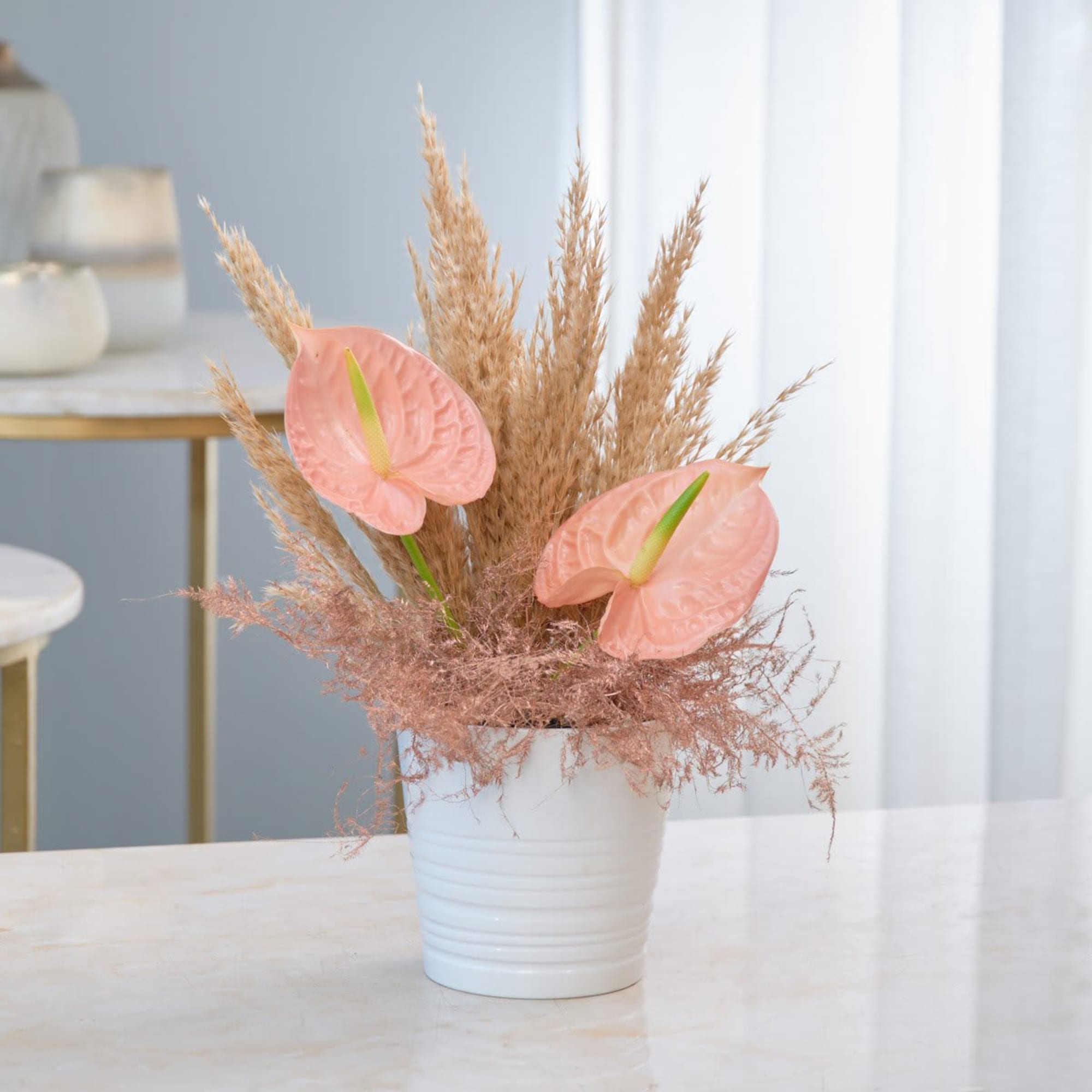 Pink anthuriums and dried grasses in a white pot