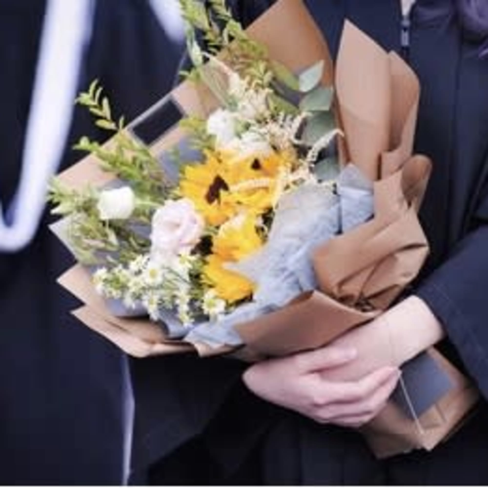 Handheld bouquet of yellow and white flowers wrapped in brown paper