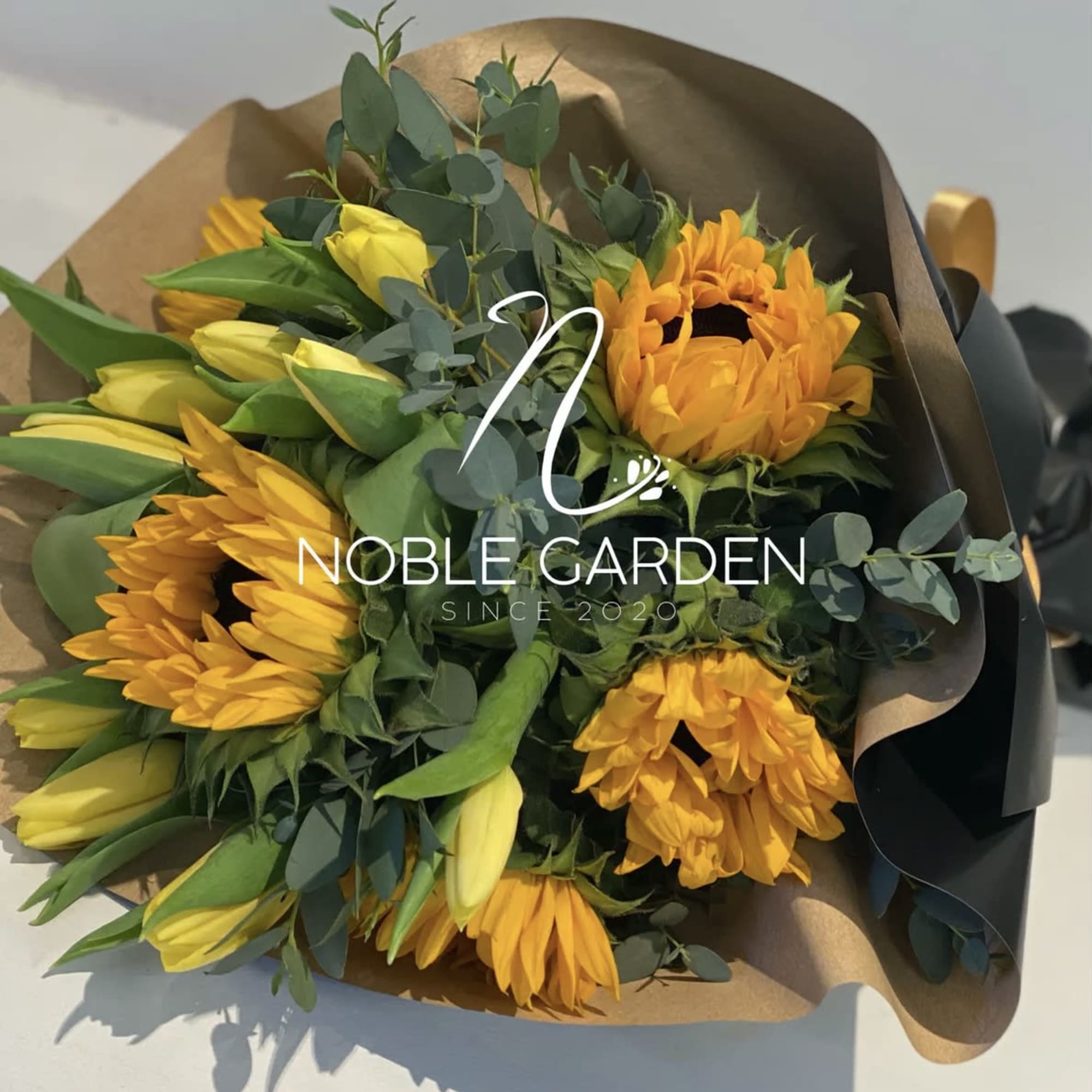 Bouquet of yellow tulips and orange sunflowers wrapped in brown paper