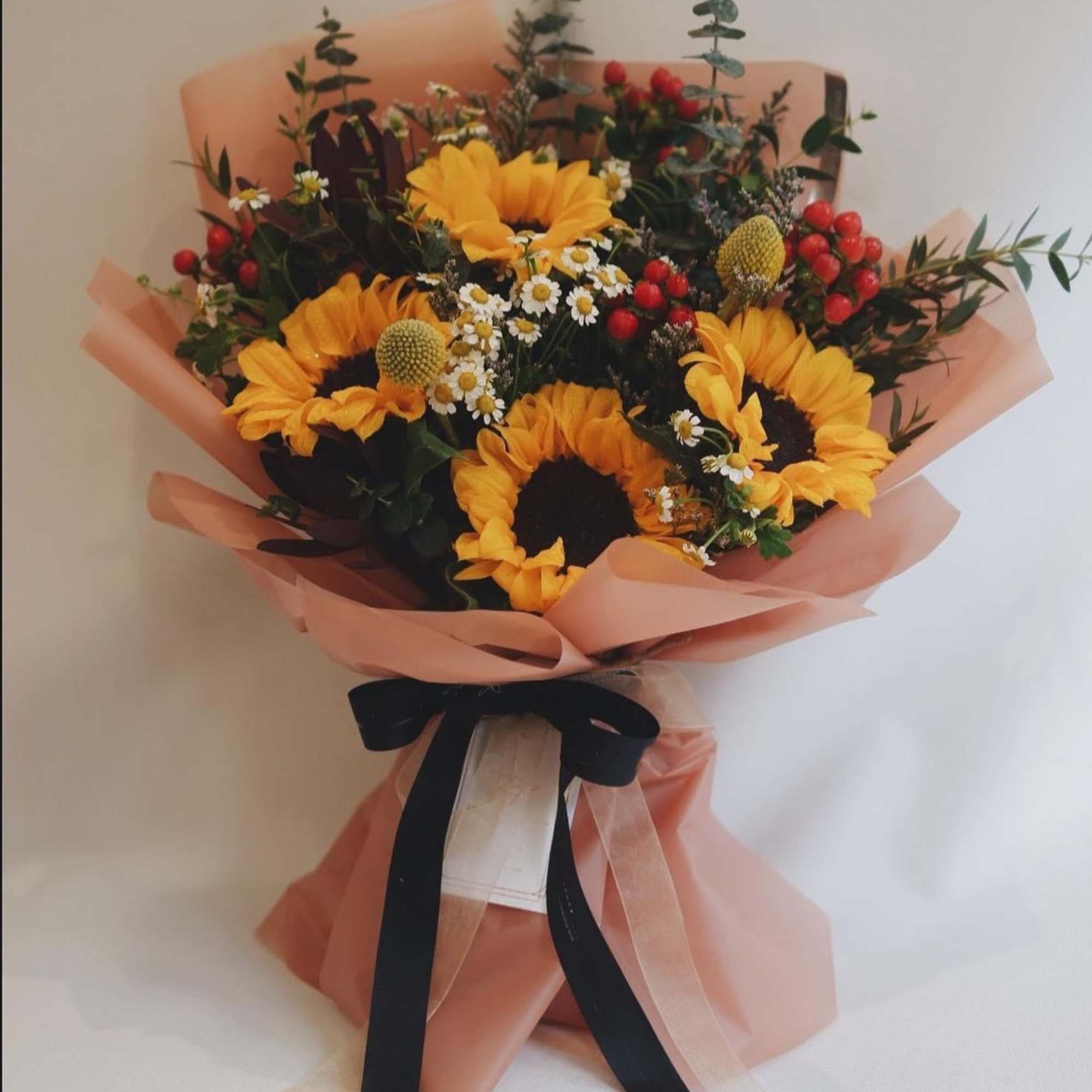 Bouquet of sunflowers with small white daisies and red berries wrapped in peach paper