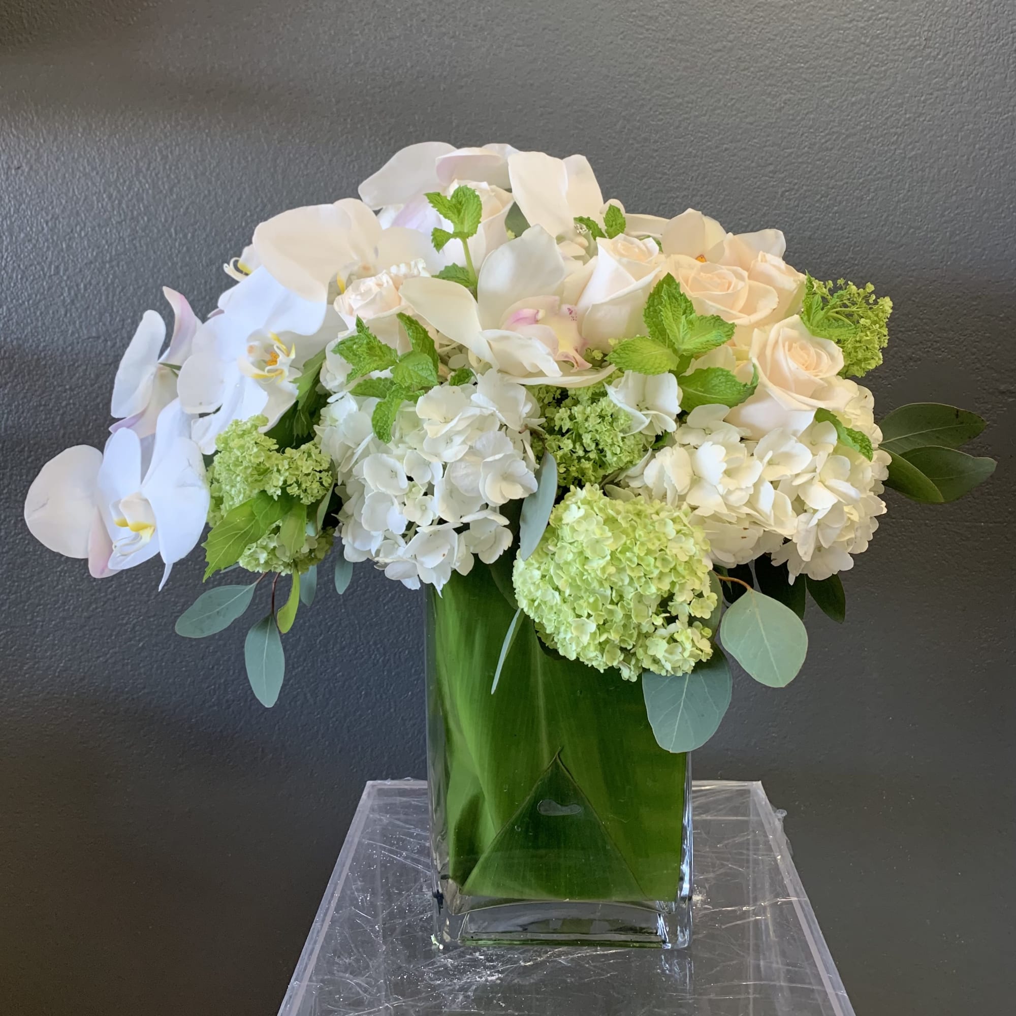 White orchids, roses, and hydrangeas in a tall glass vase