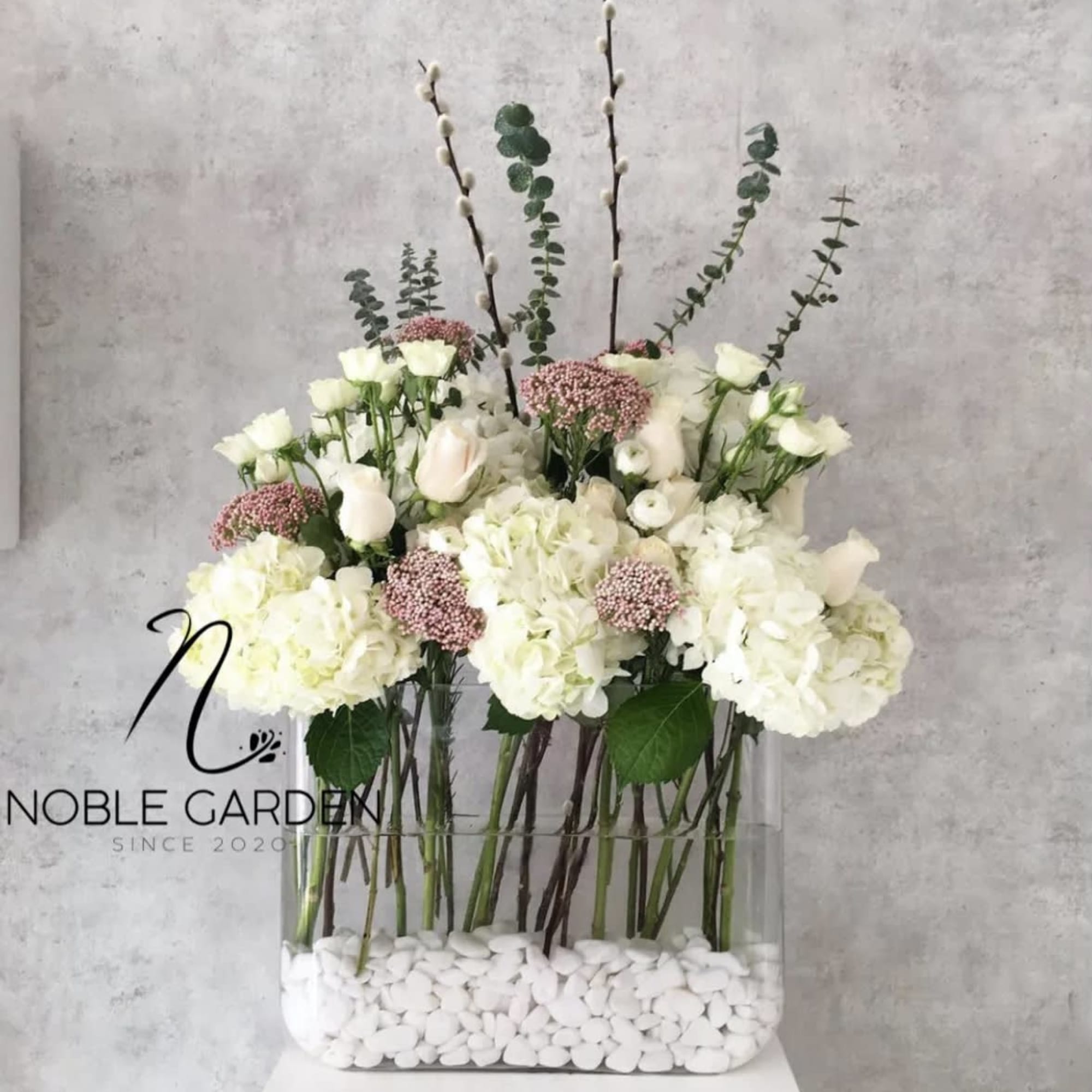 White floral arrangement in a clear rectangular vase with tall branches