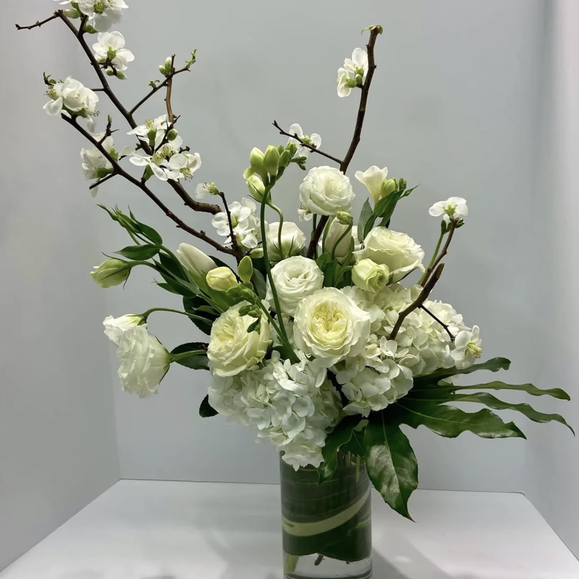 White floral arrangement in a clear glass vase with branching stems