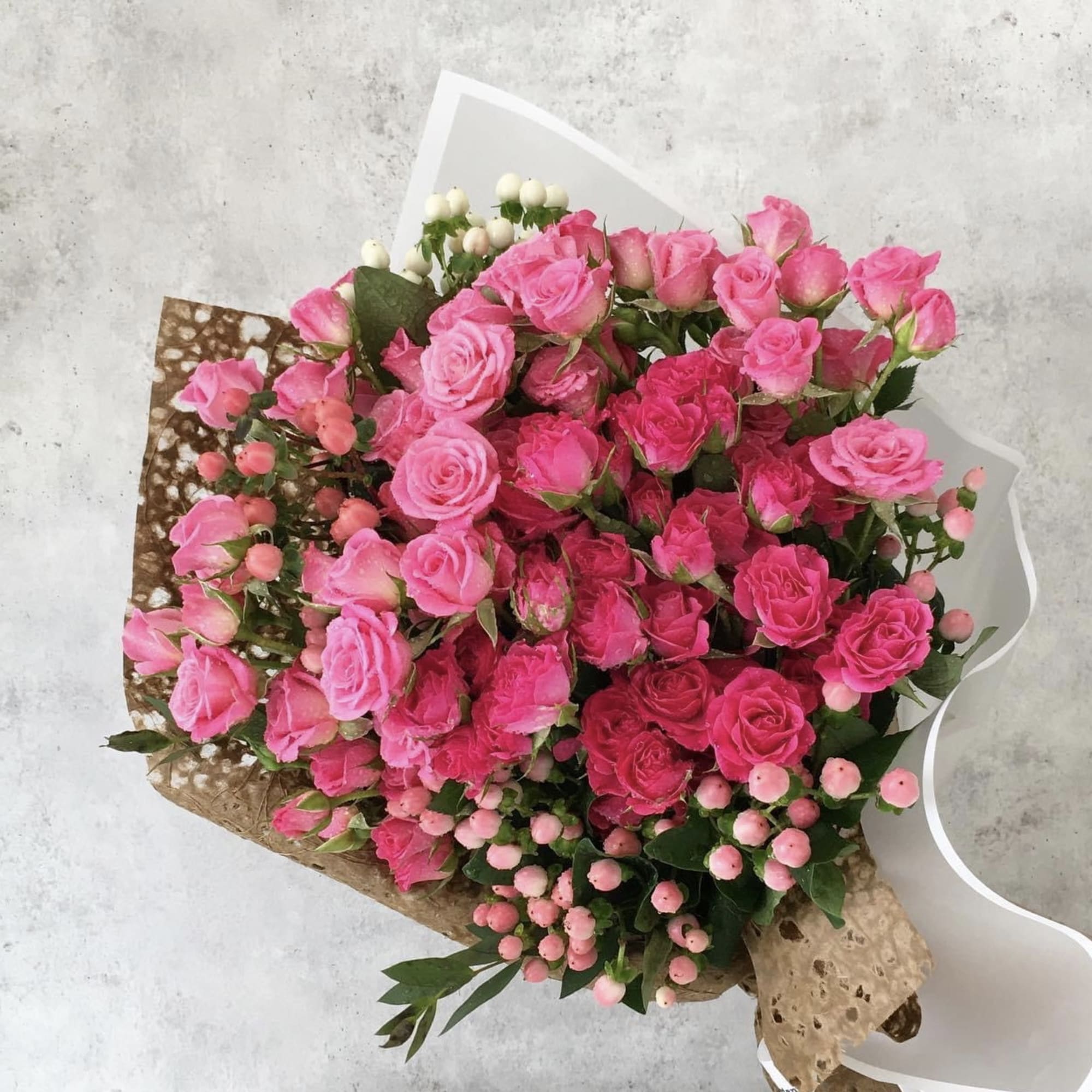Bouquet of pink roses and berry-like accents wrapped in paper