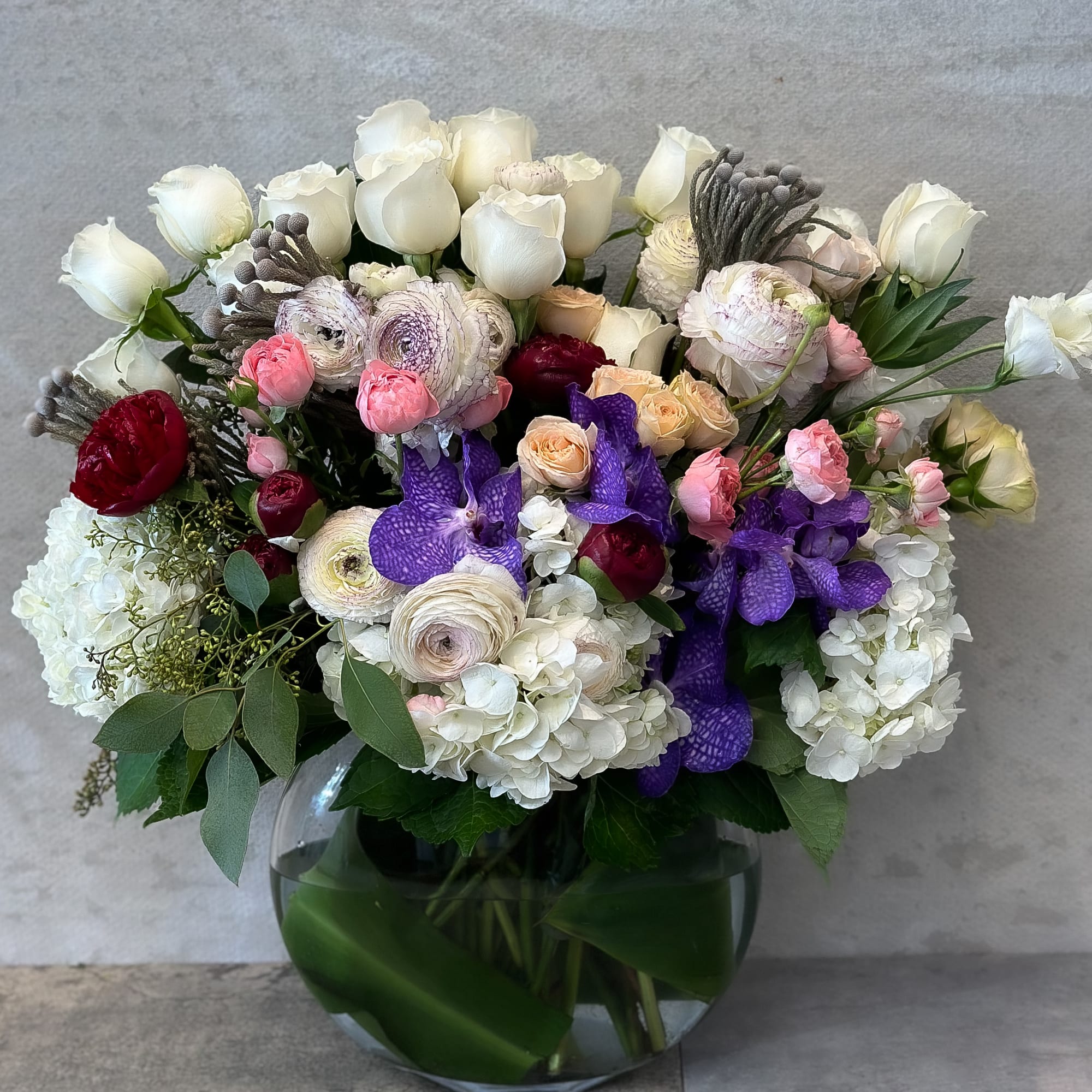 Mixed bouquet of white, pink, purple, and red flowers in a glass vase