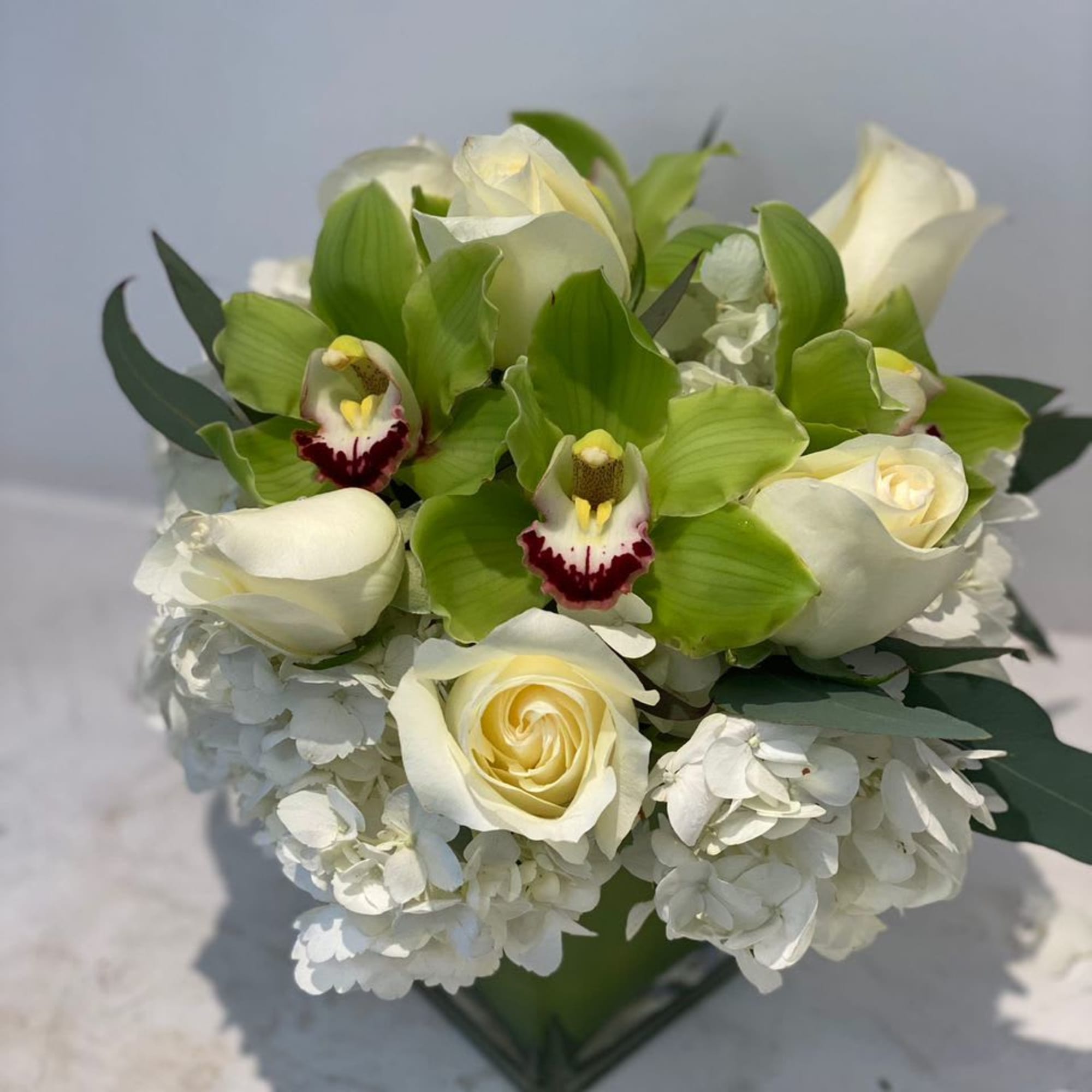 White roses and green orchids arranged with white hydrangeas