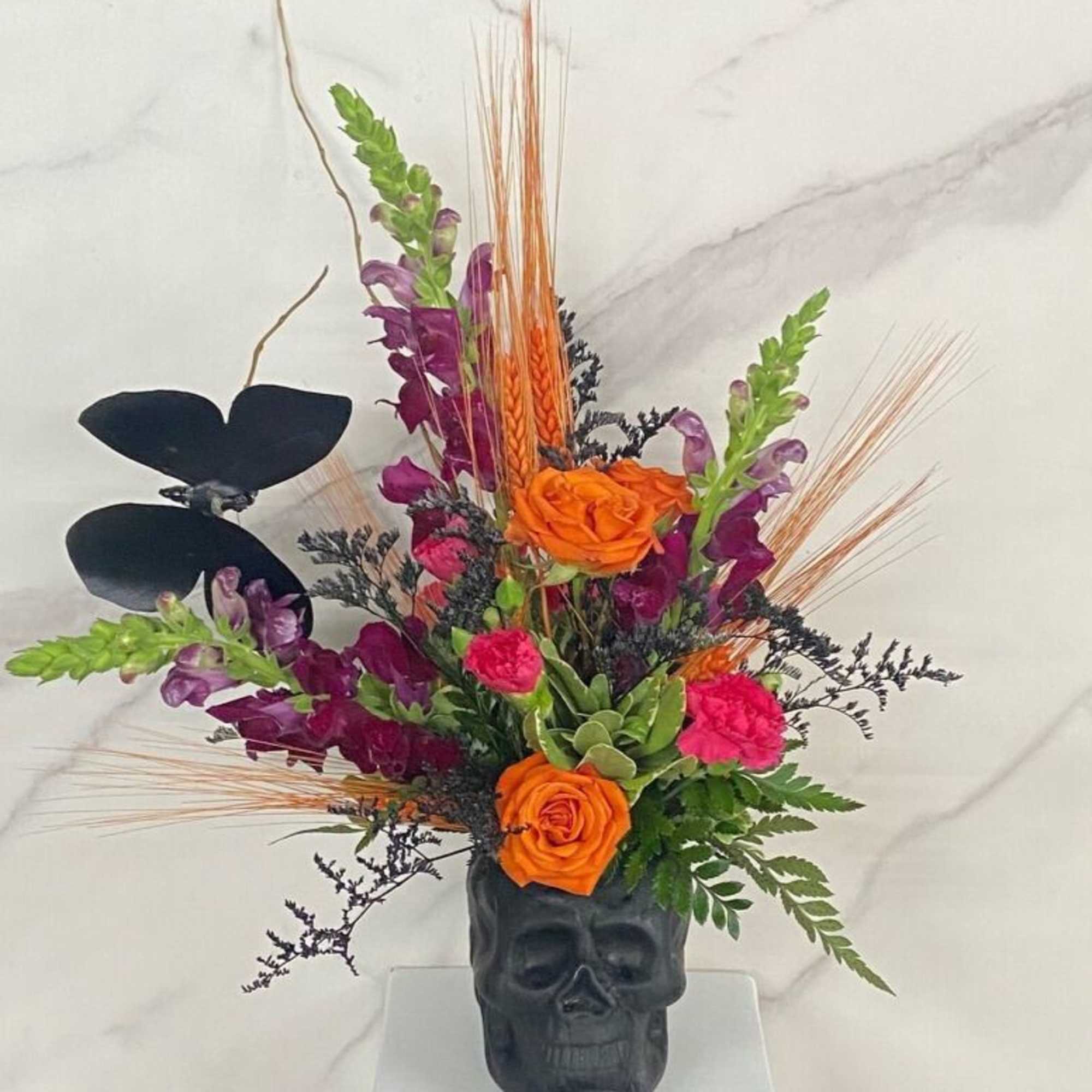 Orange and purple floral arrangement in a black skull vase, photo 2 of 2