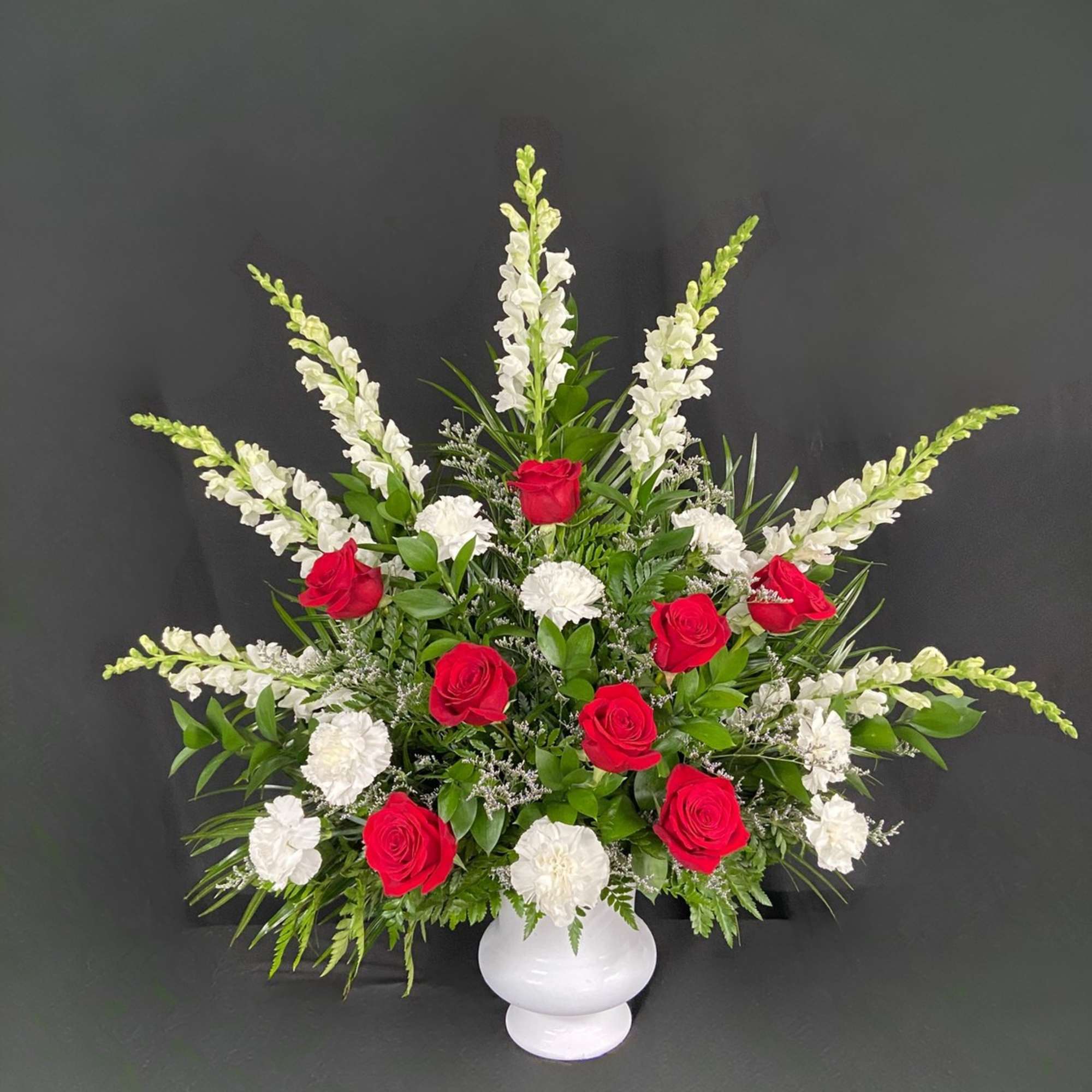 Red roses and white flowers in a white vase with greenery