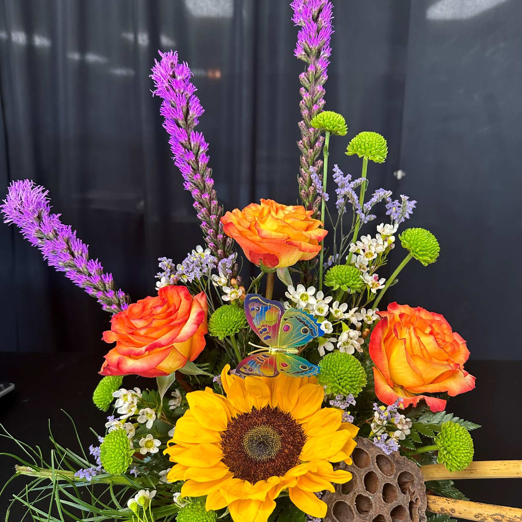 Bouquet with orange roses, a sunflower, and purple spikes in a decorative vase