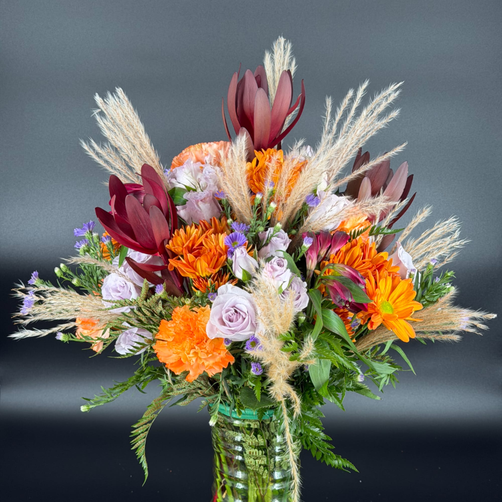 Mixed bouquet of orange, lavender, and burgundy flowers in a glass vase