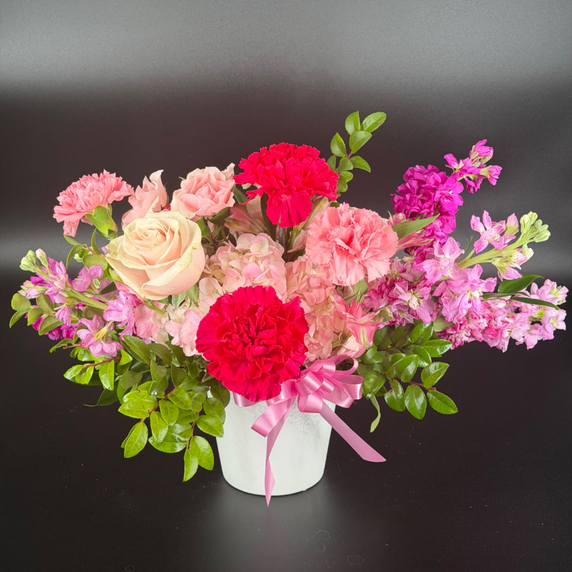 Pink and red flower arrangement in a white pot with a pink ribbon
