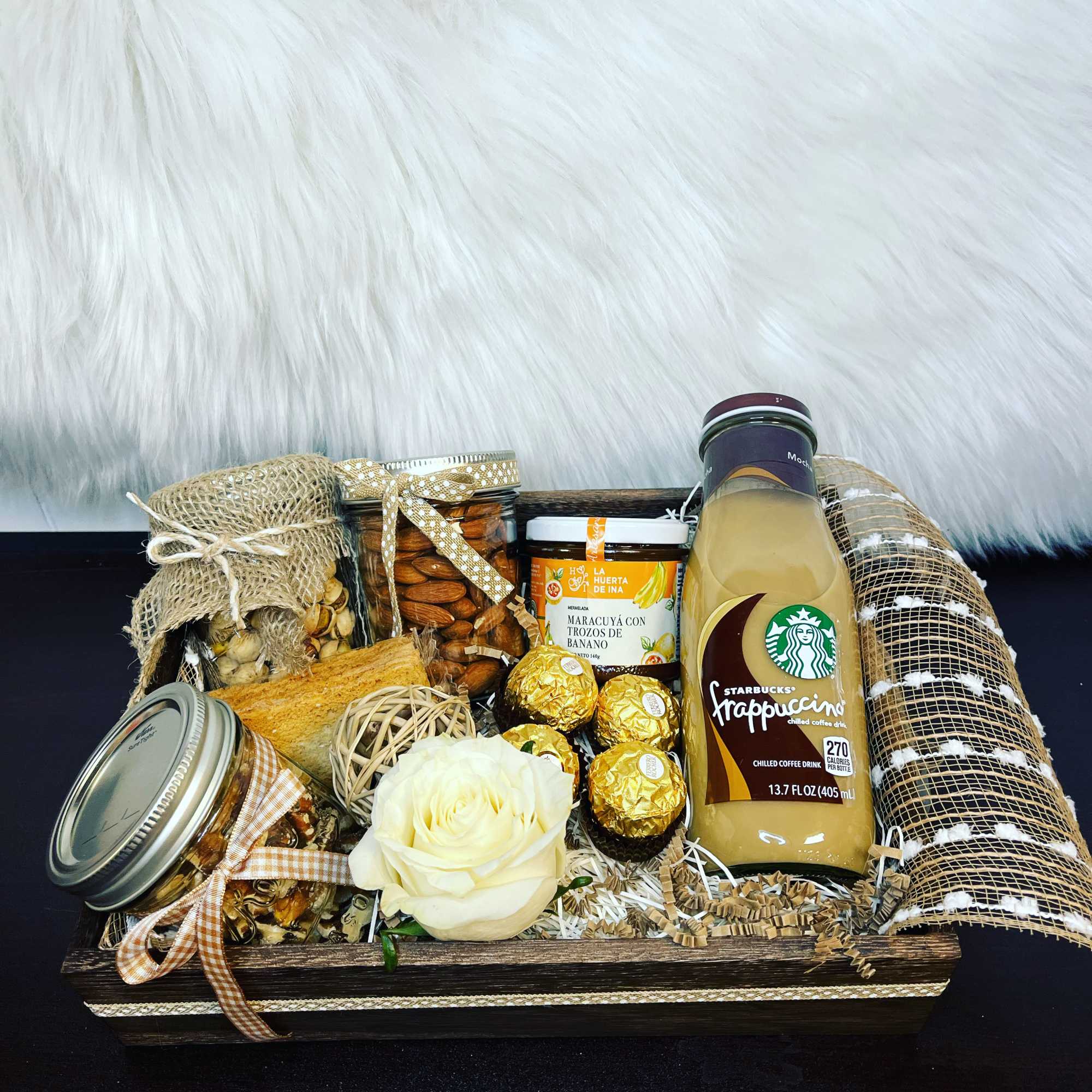 Gift basket with snacks, chocolates, coffee drink, and a white rose