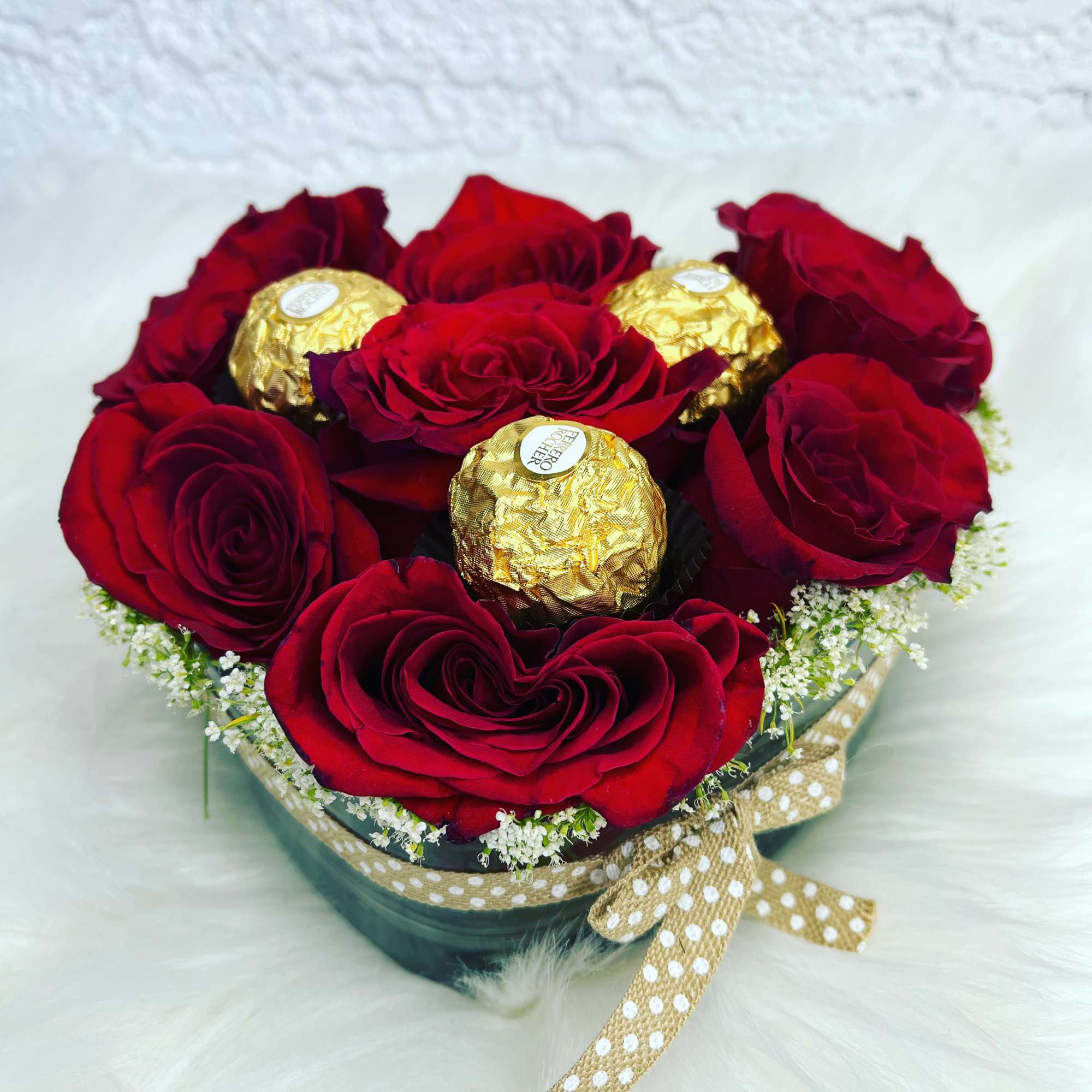 Red roses arranged with gold-wrapped chocolates in a round box
