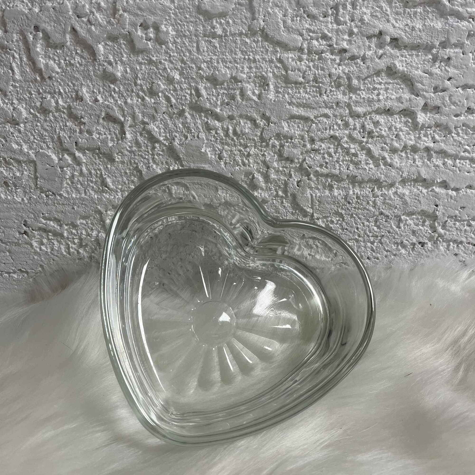 Clear glass heart-shaped dish on a white furry surface